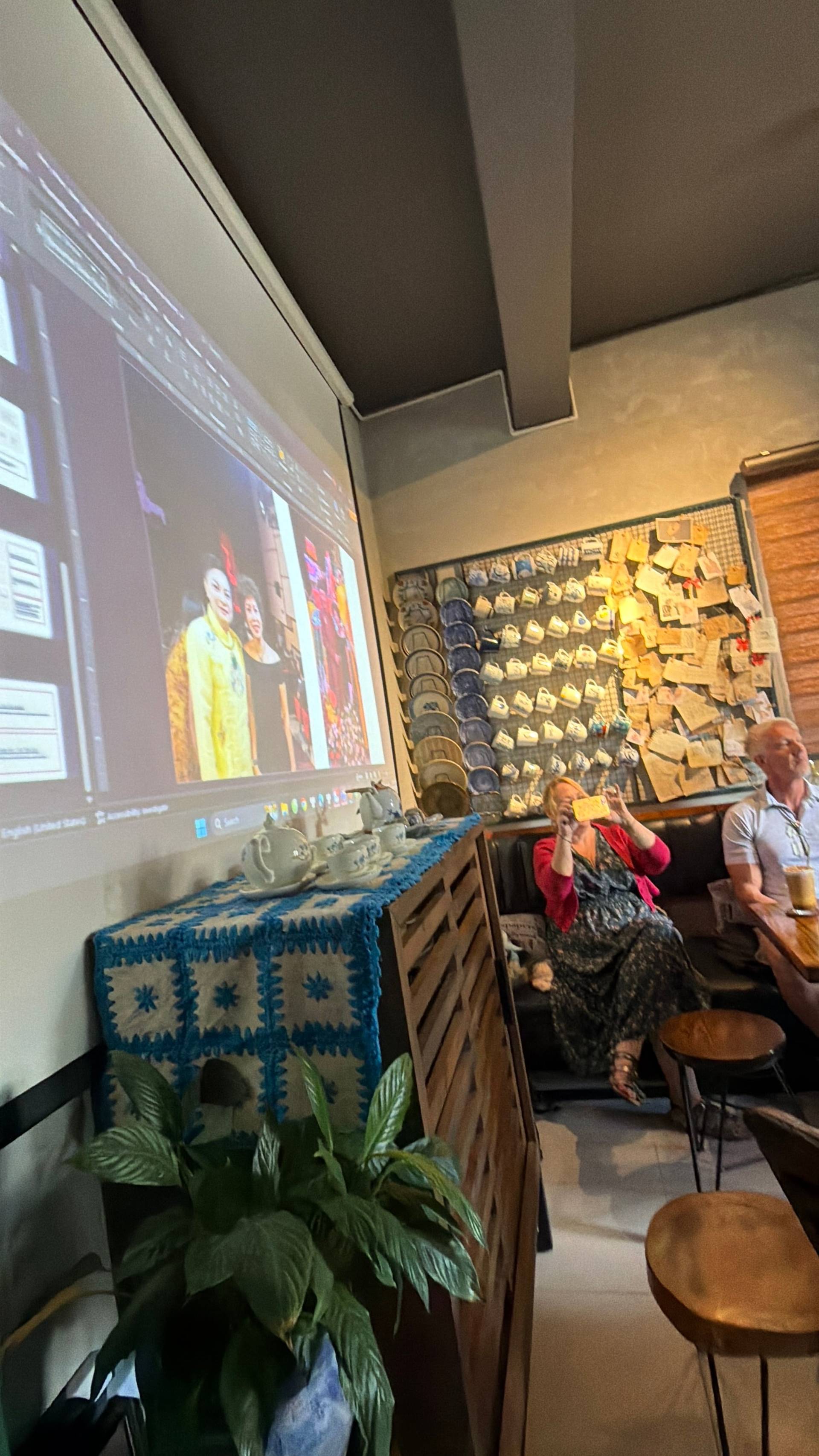 A cozy café in Đà Lạt, Vietnam, where attendees watch a presentation projected onto a large screen, surrounded by local art and decor.