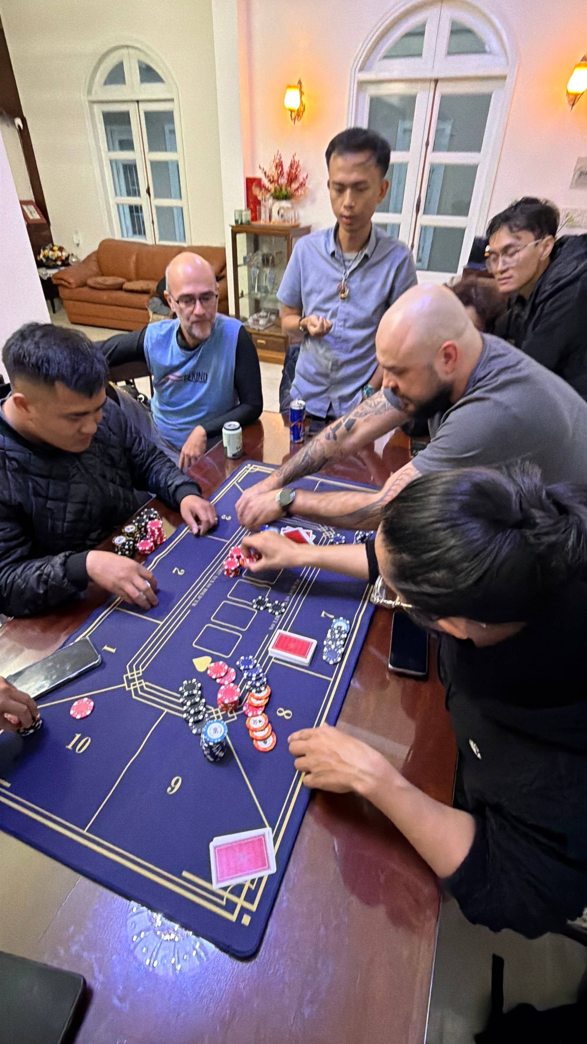 An overhead view of an active baccarat game at an elegant Đà Lạt venue, with multiple participants, poker chips, and cards arranged on a professional gaming table.