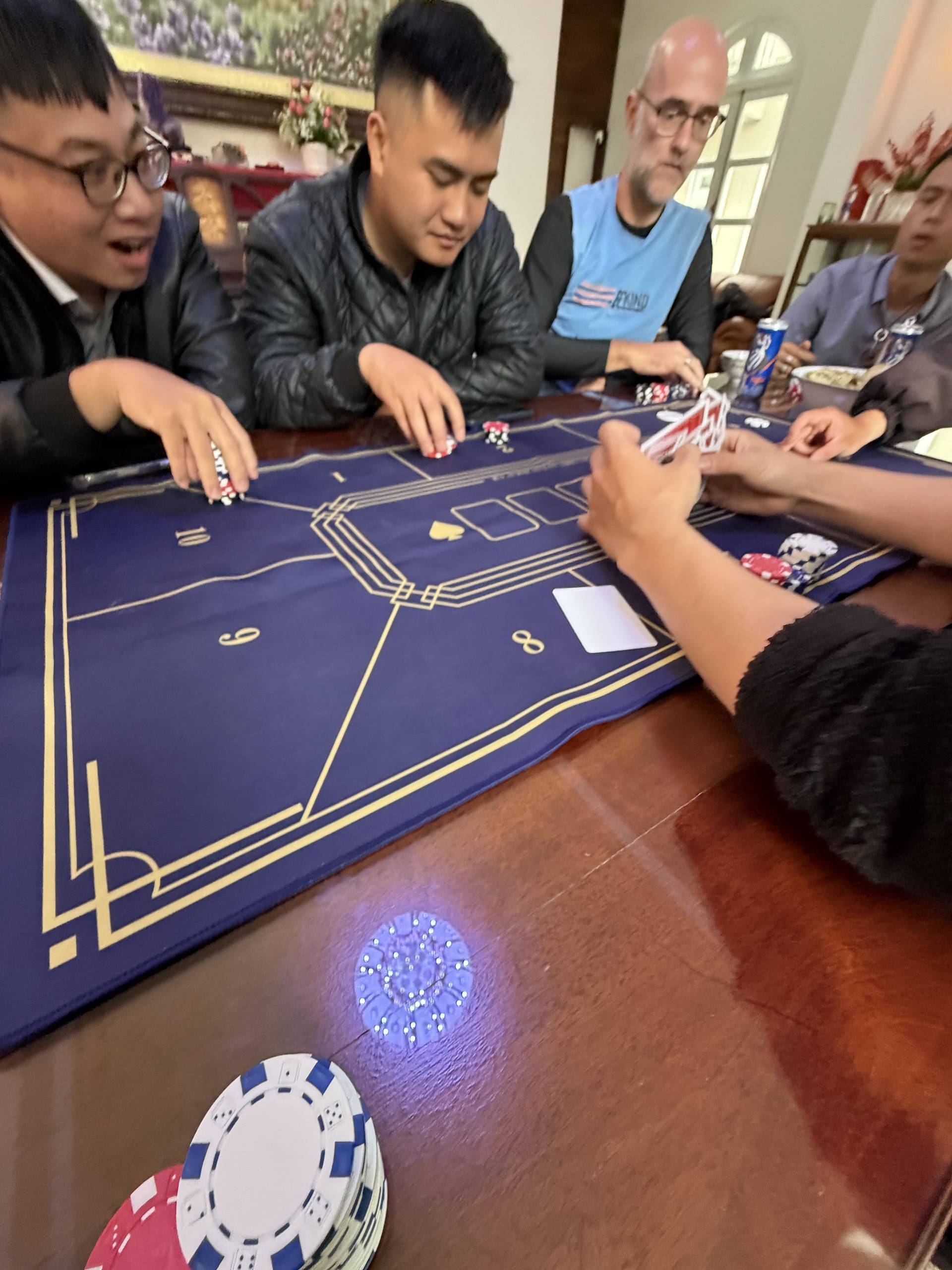 Multiple participants engage in an intense baccarat game at an upscale venue in Đà Lạt, with poker chips and cards arranged on a professional gaming table.