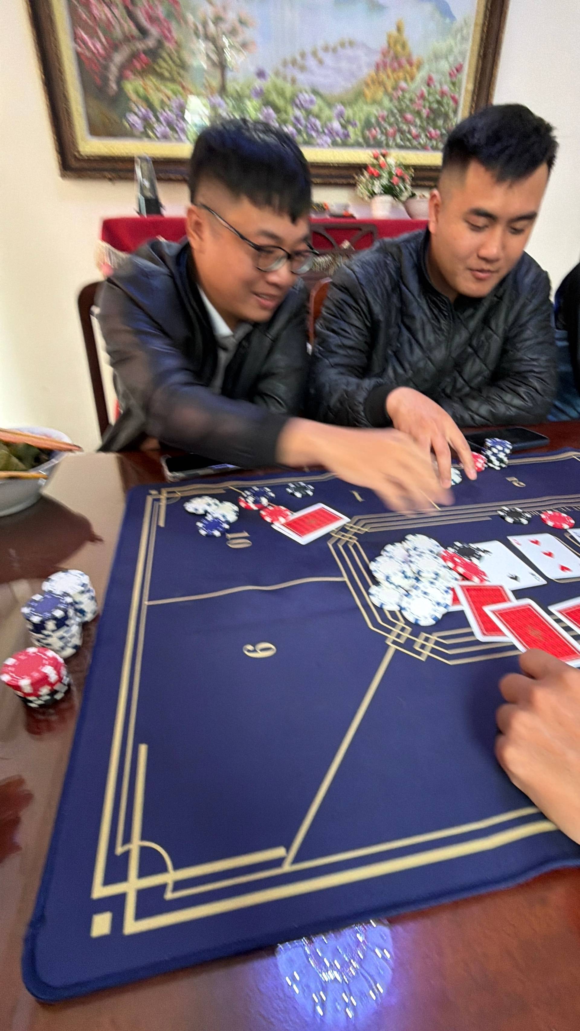 Two players focus intently on a baccarat hand at an elegant indoor gaming event, with cards and chips displayed on a professional blue table.