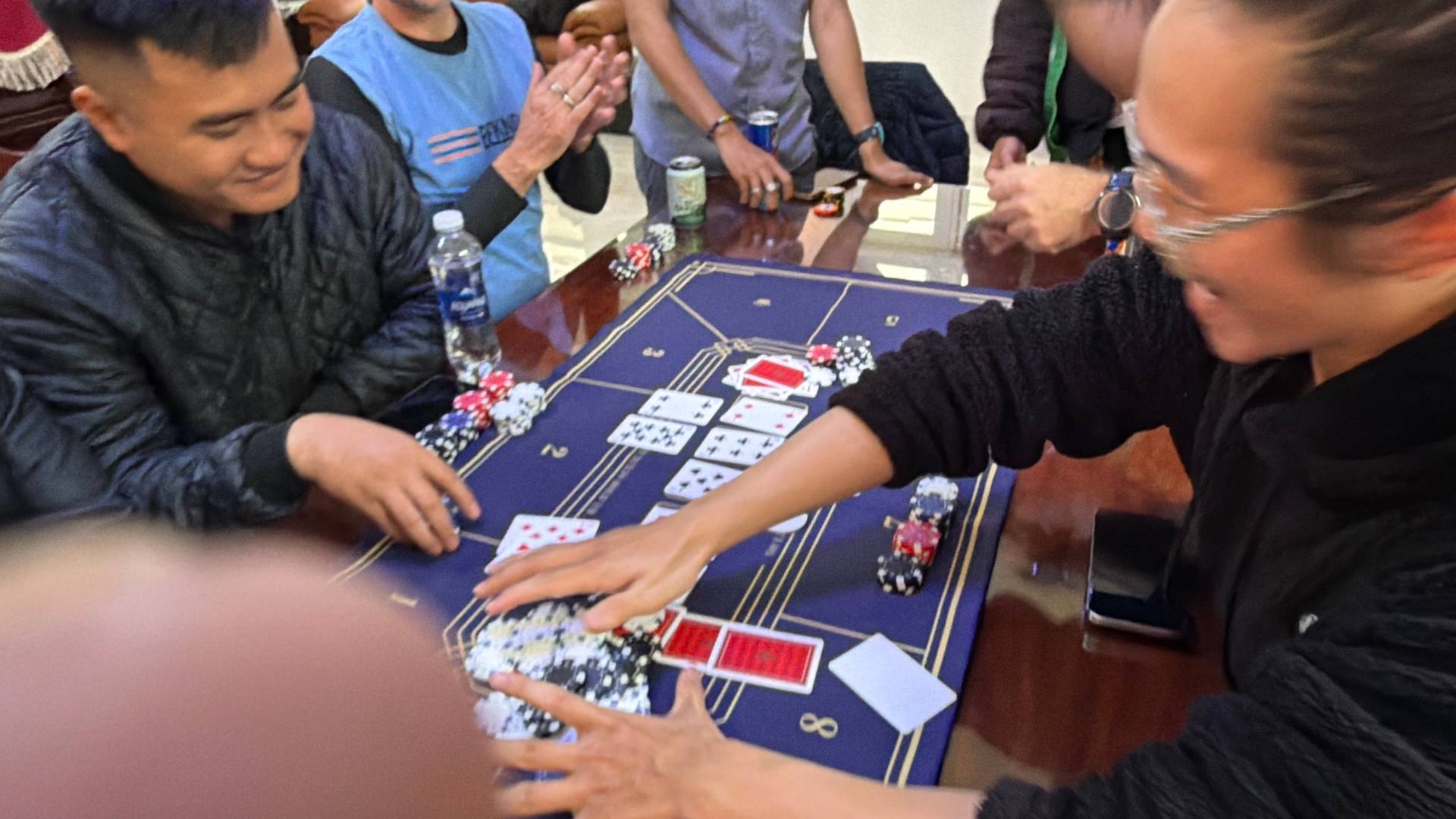 Group of players gathered around a baccarat table with cards and poker chips, engaged in social card gaming during an event gathering in Đà Lạt.