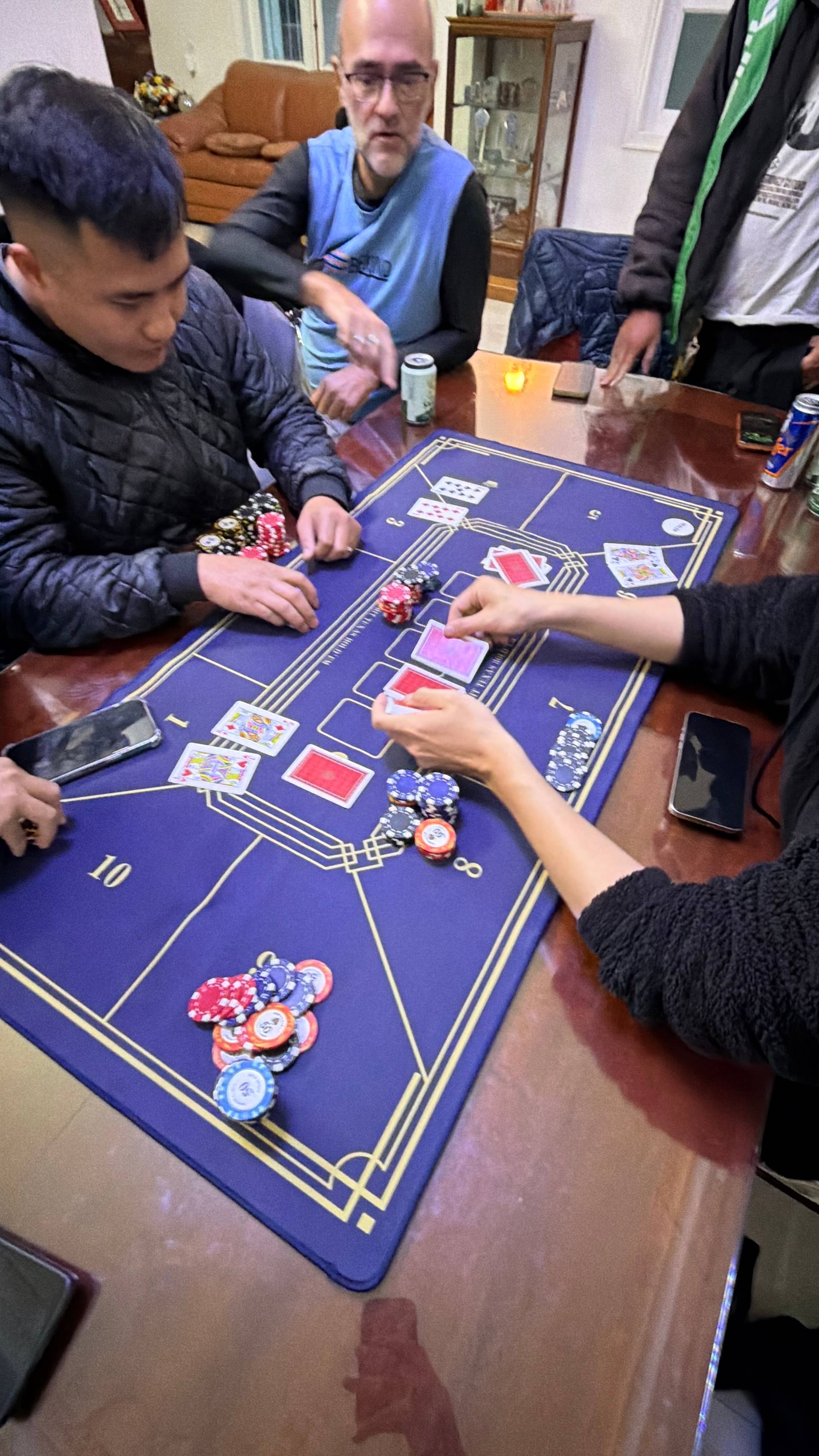 Active baccarat game with multiple players around a professional gaming table, showing cards and poker chips during casual gaming event in Đà Lạt.