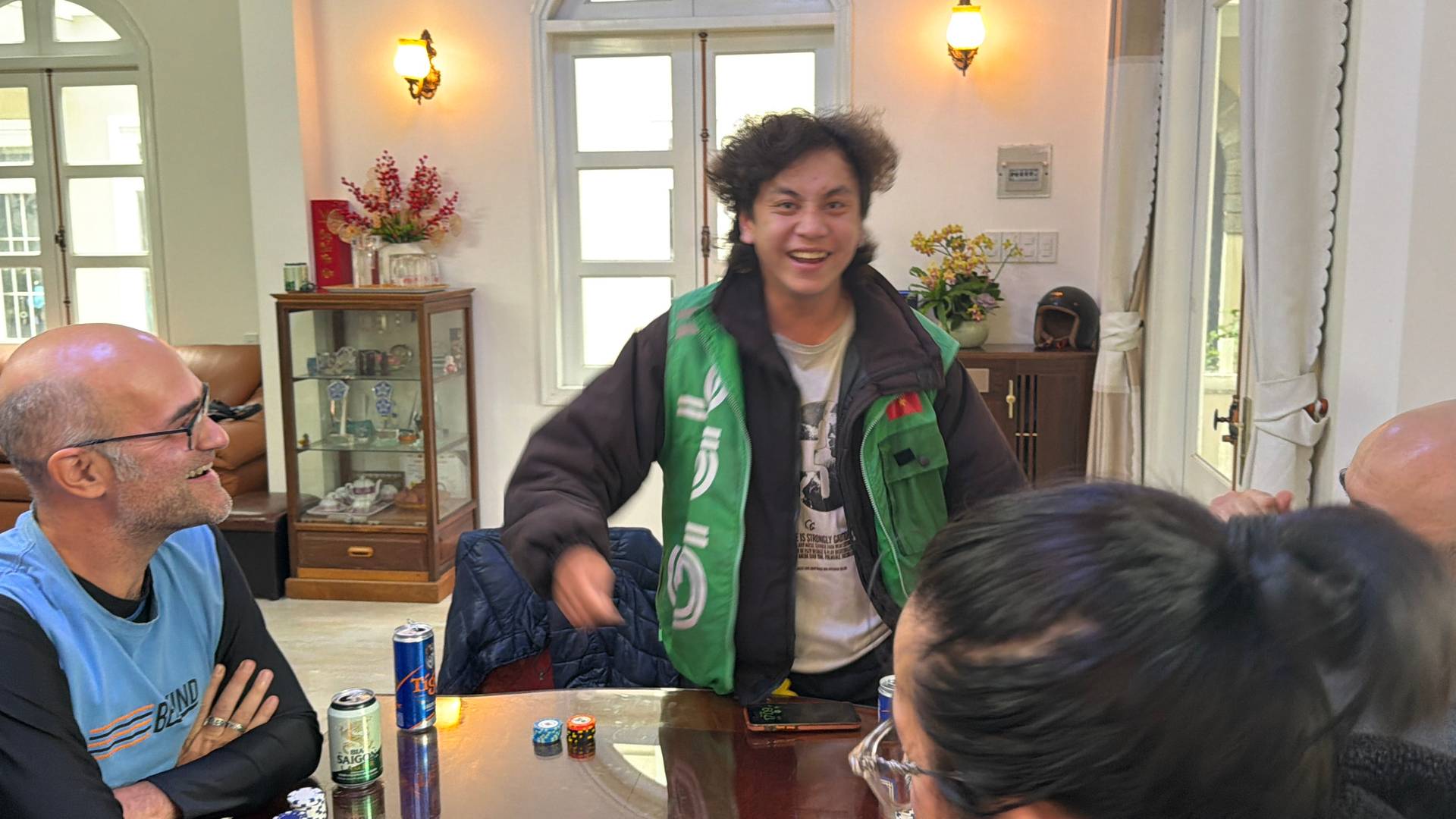 Casual social gathering in an elegant modern home in Đà Lạt, with a group gathered around a table enjoying beverages and friendly conversation in a refined interior setting.