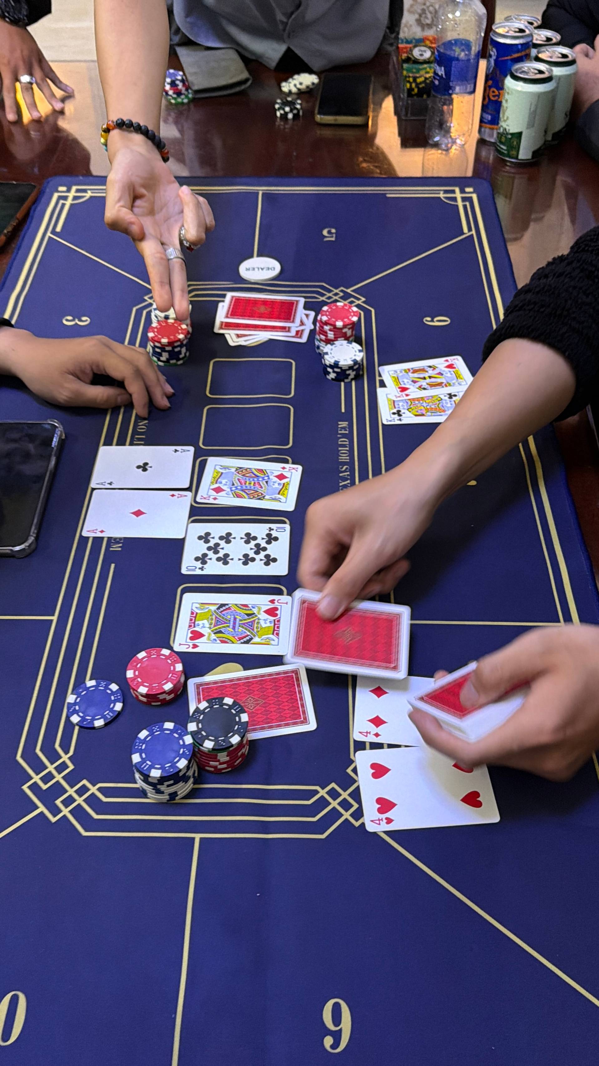 An intimate close-up of baccarat gameplay showing hands, cards, and stacked poker chips in multiple colors arranged on a professional blue gaming table at a Đà Lạt event.