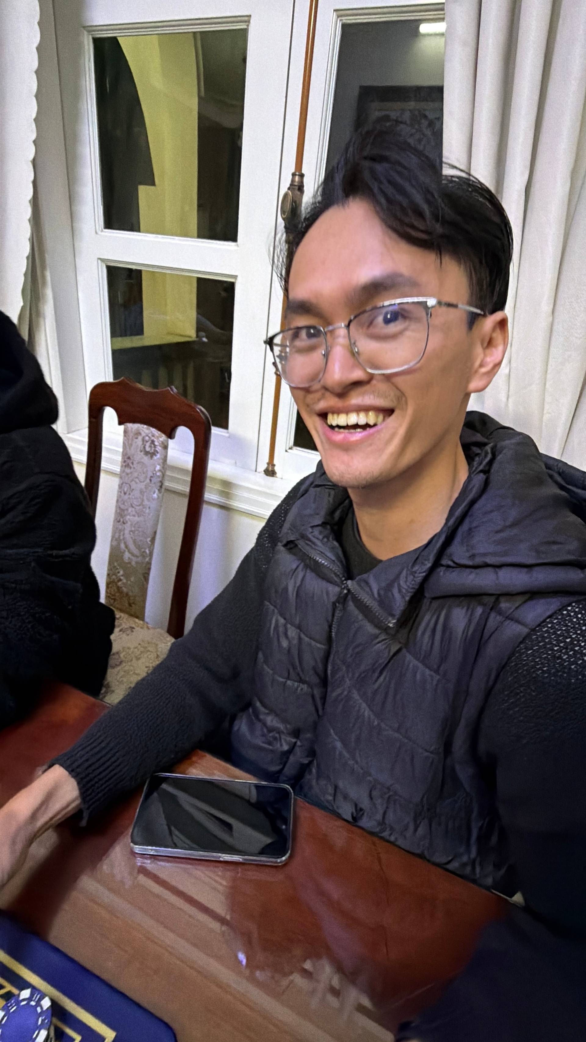 A smiling participant enjoys the evening card game event in a Đà Lạt villa interior, capturing the warm hospitality and fun atmosphere of the gathering.
