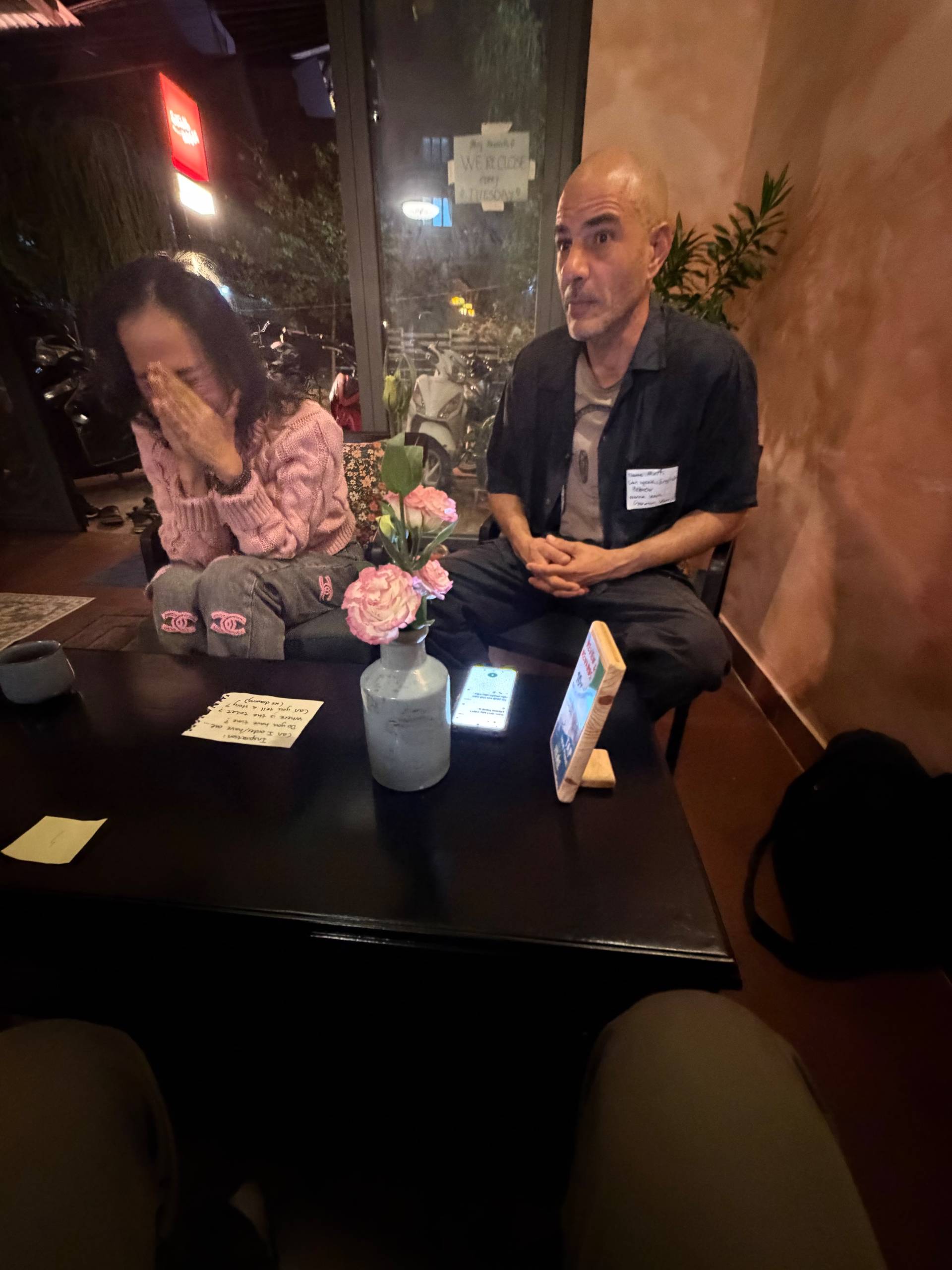 Two individuals seated in a cozy café setting in Đà Lạt, Vietnam, engaged in conversation with a relaxed and intimate atmosphere.