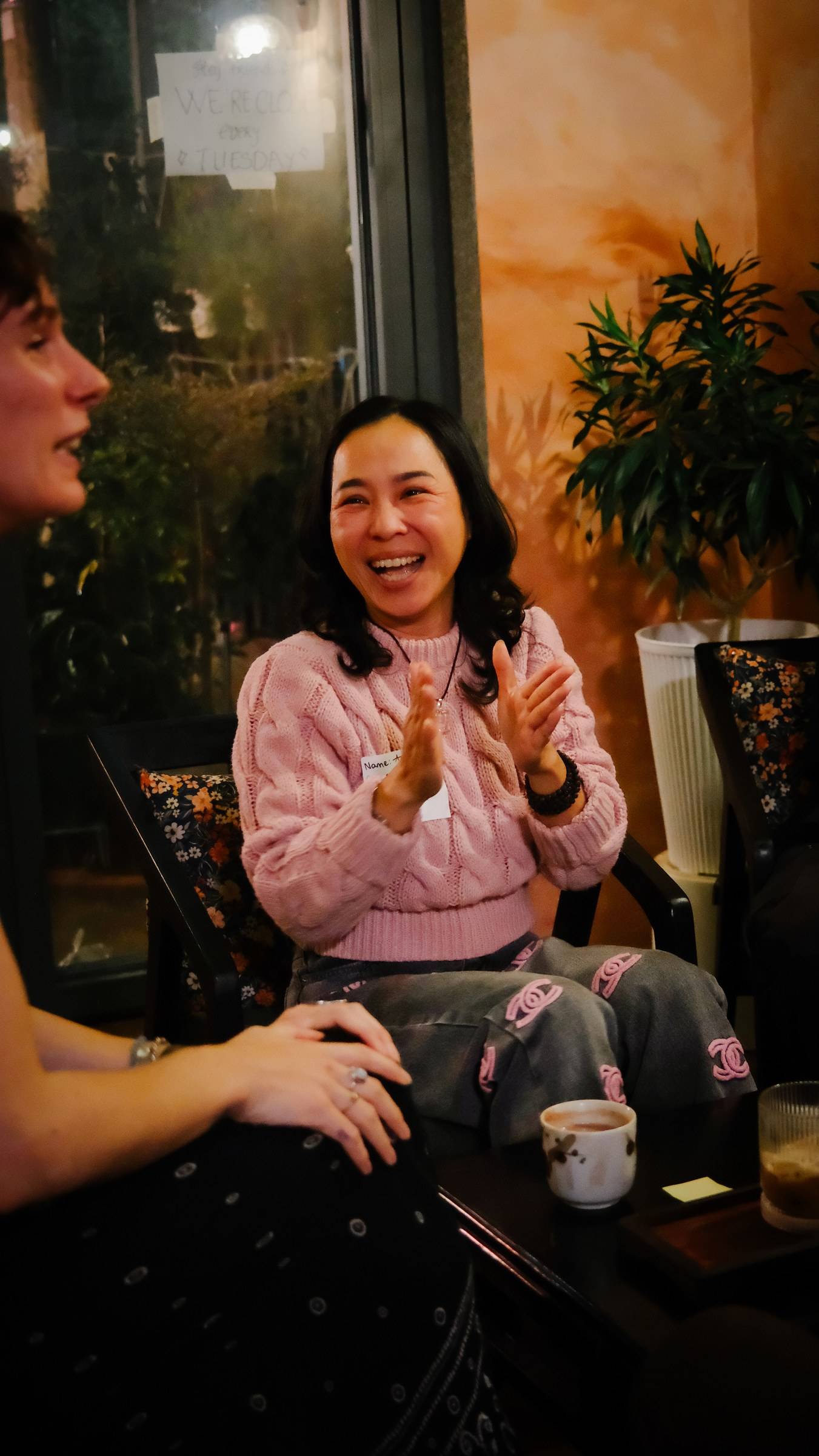 Two friends share a joyful moment in a cozy café setting in Đà Lạt, Vietnam, with warm lighting and a relaxed atmosphere.
