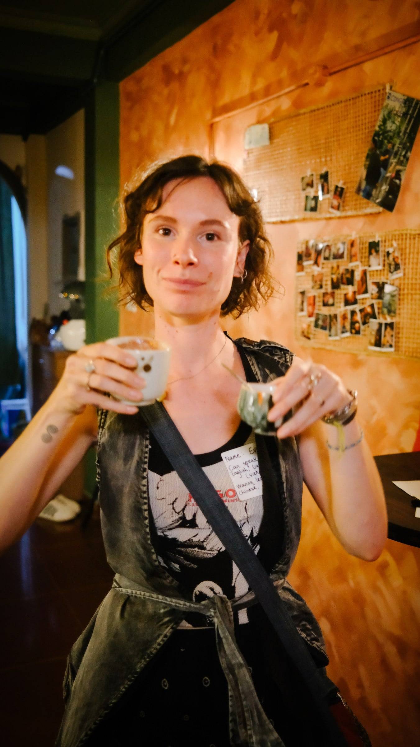 A person enjoying a drink in a cozy café setting with warm lighting and personal photos displayed on the wall behind them.