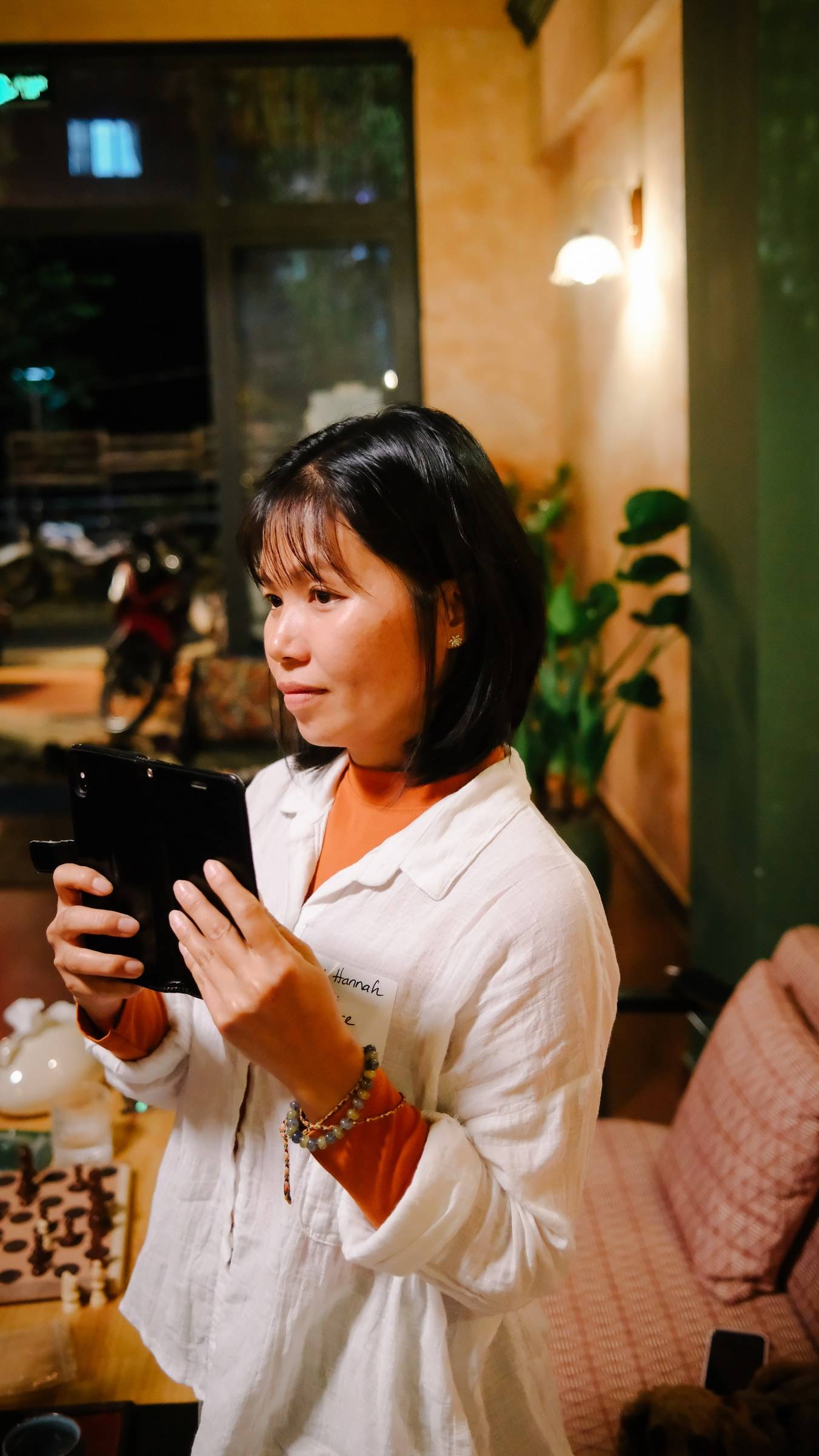 A woman is engrossed in her tablet within a cozy café setting in Đà Lạt, Vietnam, surrounded by warm lighting and greenery.