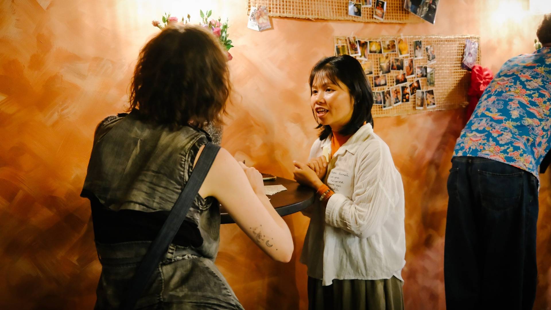 A warm, intimate scene in Đà Lạt where two individuals engage in conversation over a table, surrounded by personal photos and vibrant decor that reflects local culture.