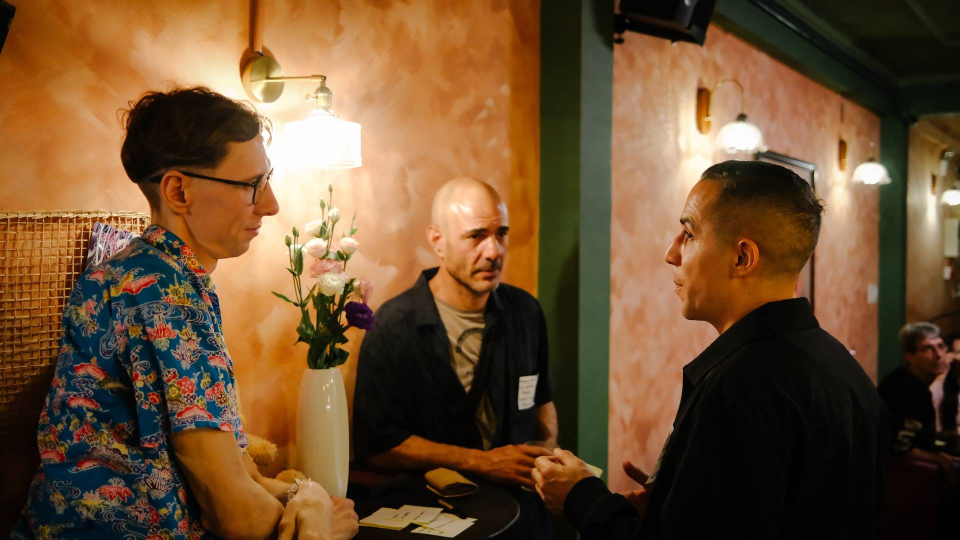 A group of individuals engaged in conversation within a warmly lit indoor setting, likely part of a social gathering or event in Đà Lạt.