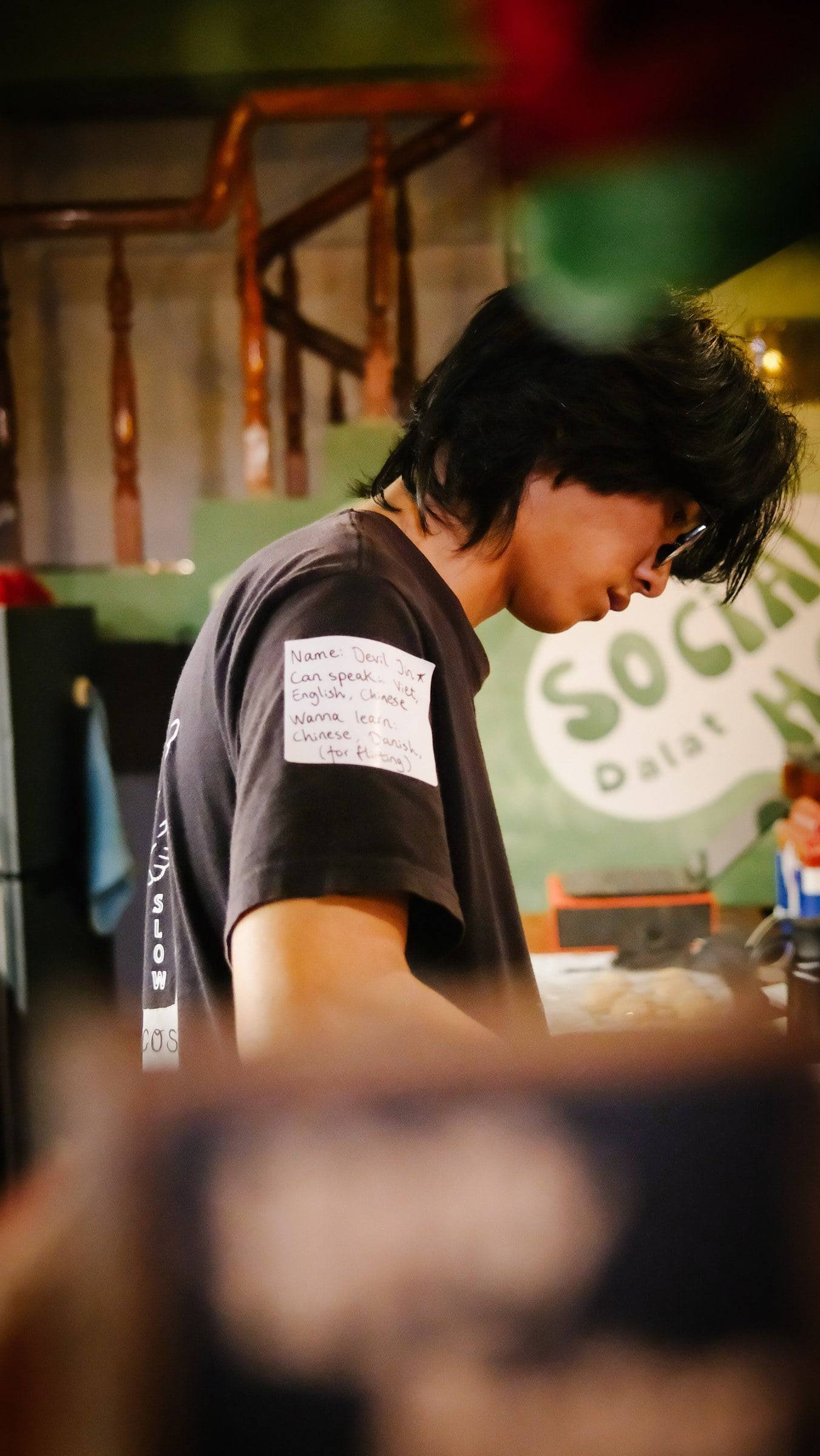 A young person is focused on a task in a social setting in Đà Lạt, Vietnam, with a relaxed and casual atmosphere.