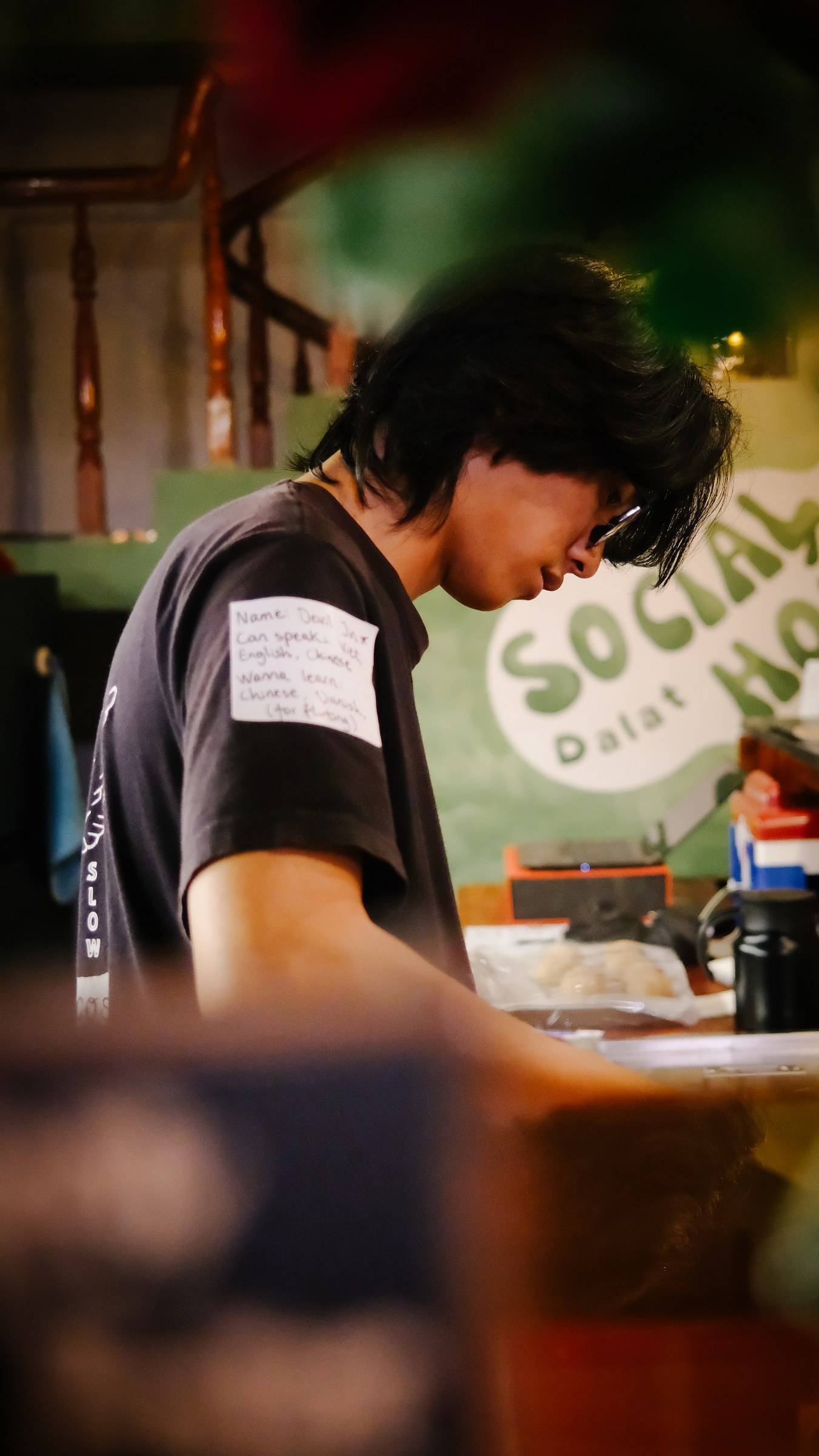 A person wearing a t-shirt with language proficiency details is engaged in a casual activity at a social hub in Đà Lạt, Vietnam.