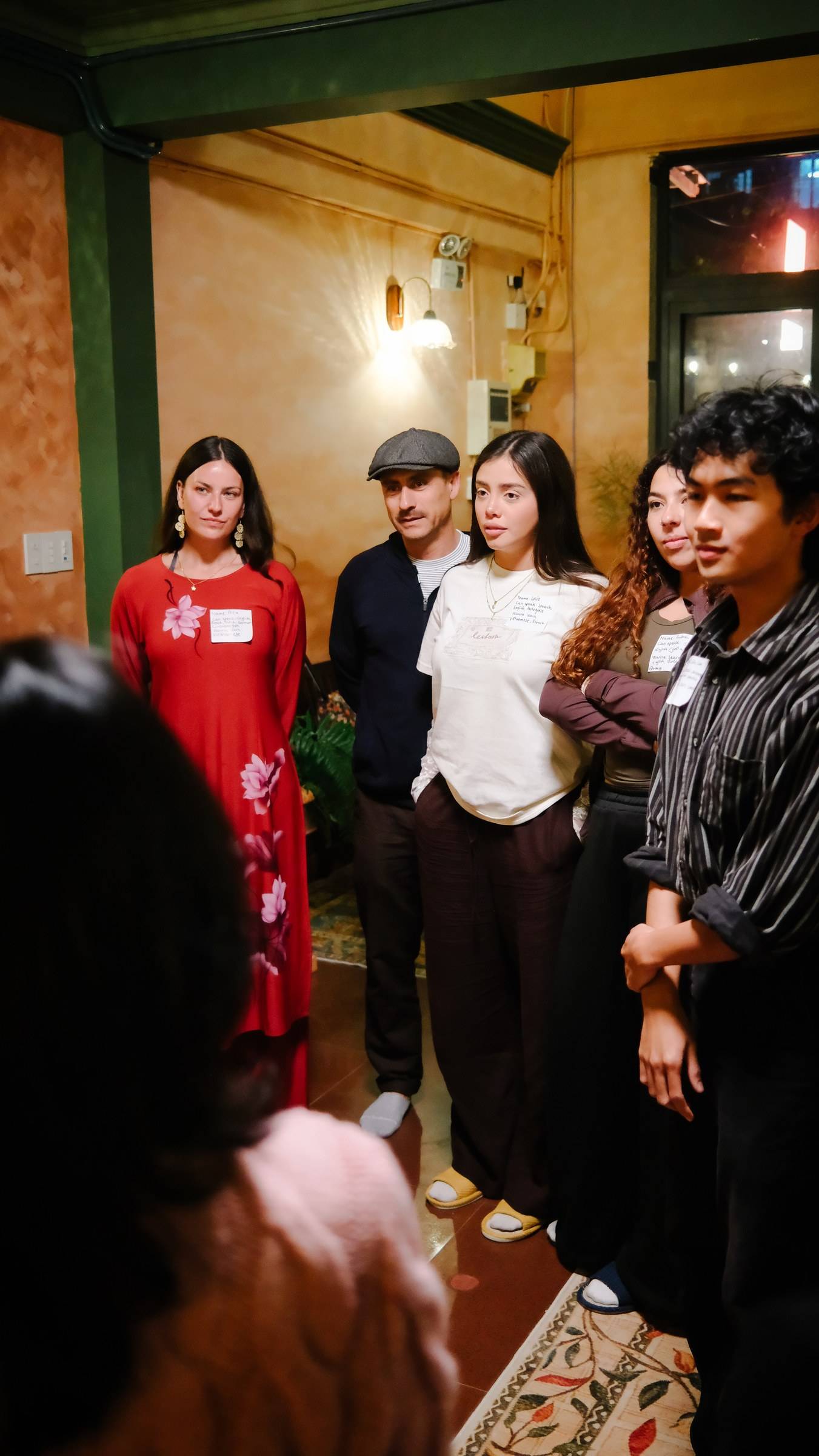 A group of individuals stands together in a warmly lit indoor setting, possibly during a social gathering or community event in Đà Lạt, Vietnam.