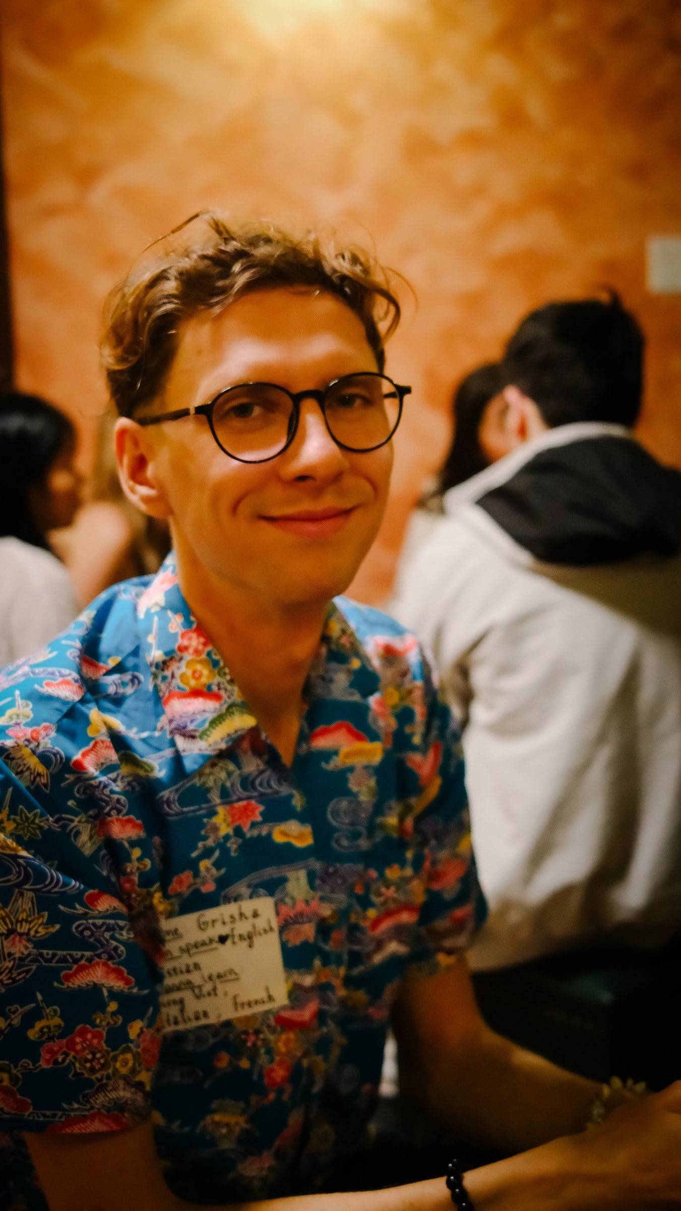A vibrant scene in Đà Lạt, Vietnam, featuring a person wearing a colorful floral shirt and smiling amidst a lively gathering with warm lighting.