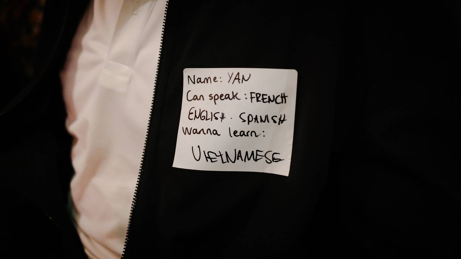 A close-up of a note pinned to someone's jacket in Đà Lạt, Vietnam, indicating their language skills and interest in learning Vietnamese.
