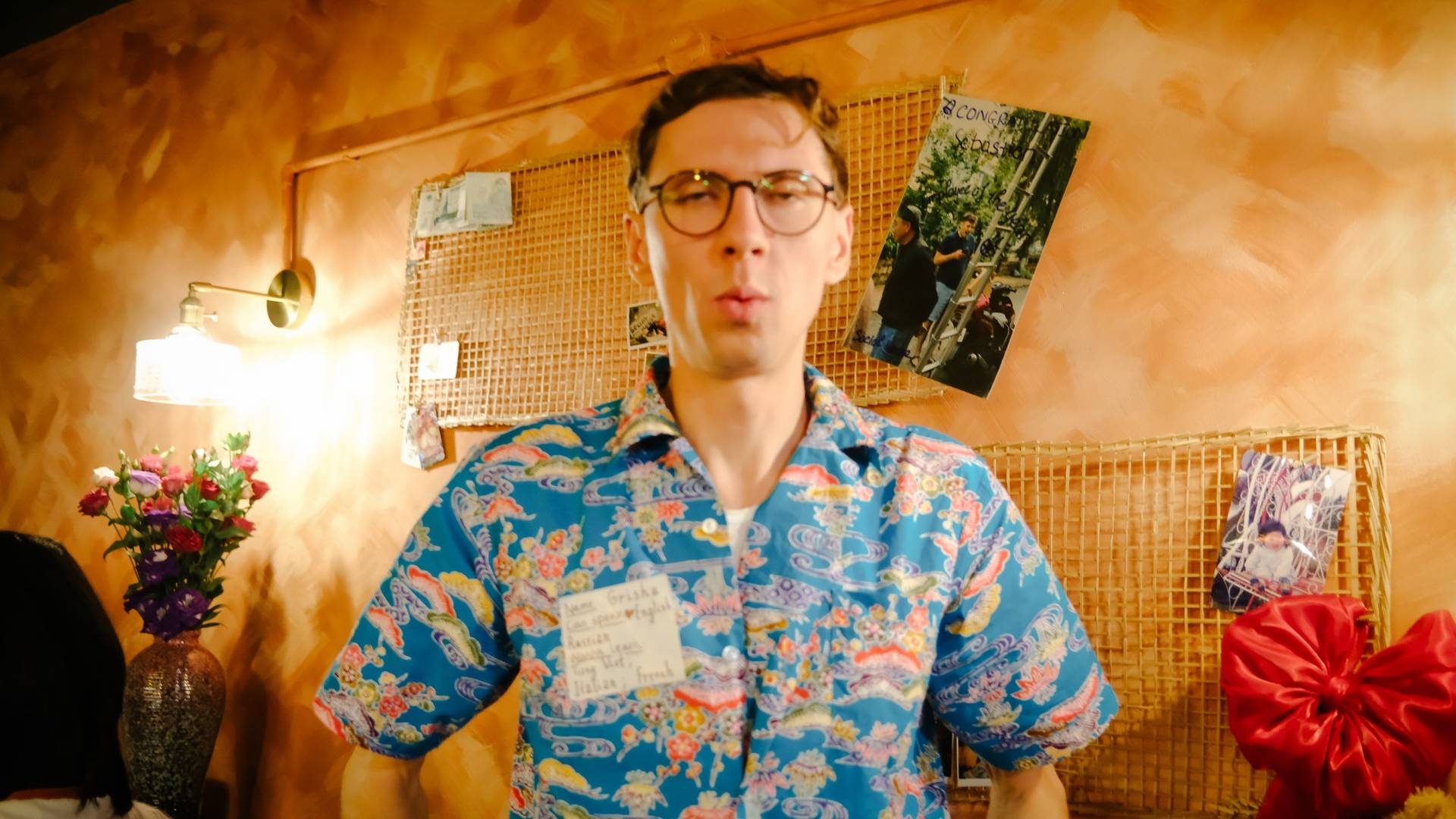 A vibrant scene in Đà Lạt, Vietnam, featuring a person wearing a colorful floral shirt with a name tag, surrounded by personal photos and decorations that evoke a warm, nostalgic atmosphere.