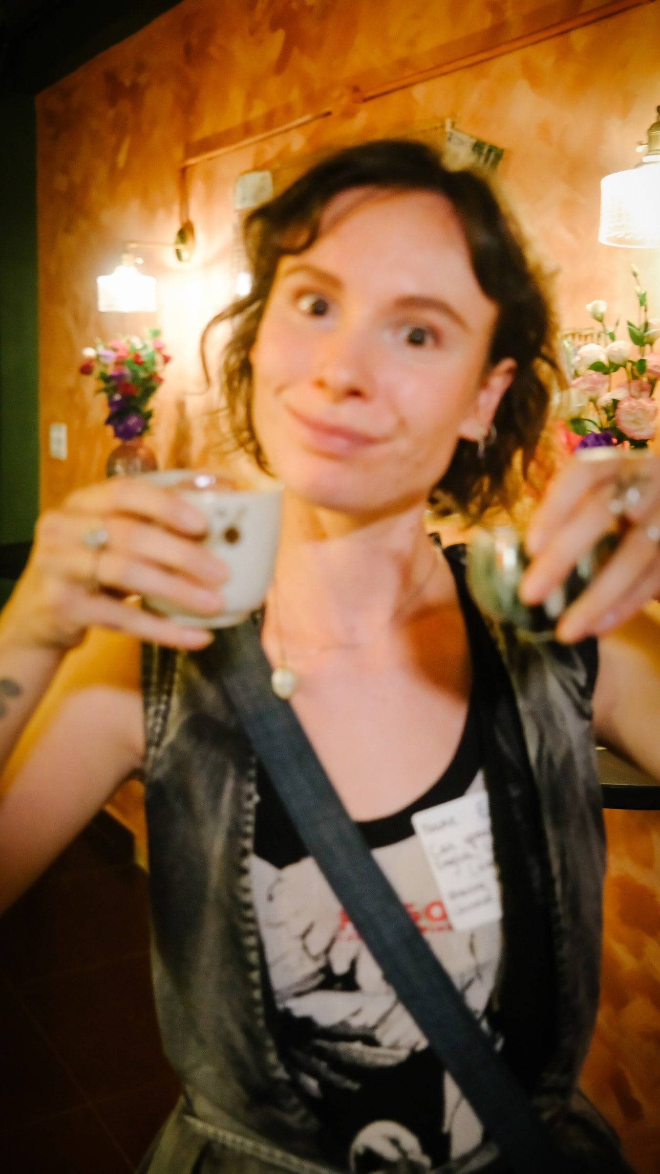 A person enjoying a drink in a cozy café setting with warm lighting and floral decorations, reflecting a relaxed and joyful atmosphere.