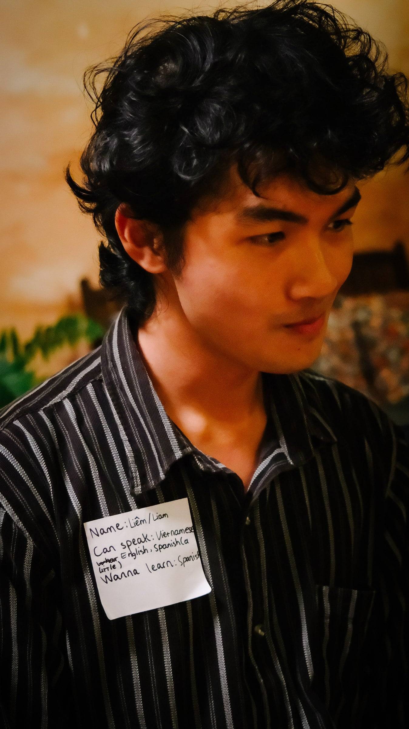 A person wearing a striped shirt with a name tag indicating they can speak Vietnamese and English, and want to learn Spanish at an event in Đà Lạt, Vietnam.