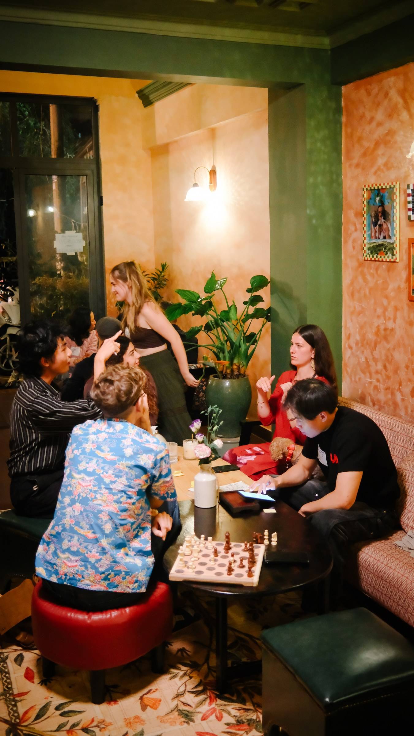 A lively gathering of friends in a cozy café in Đà Lạt, Vietnam, enjoying board games and laughter under warm lighting.