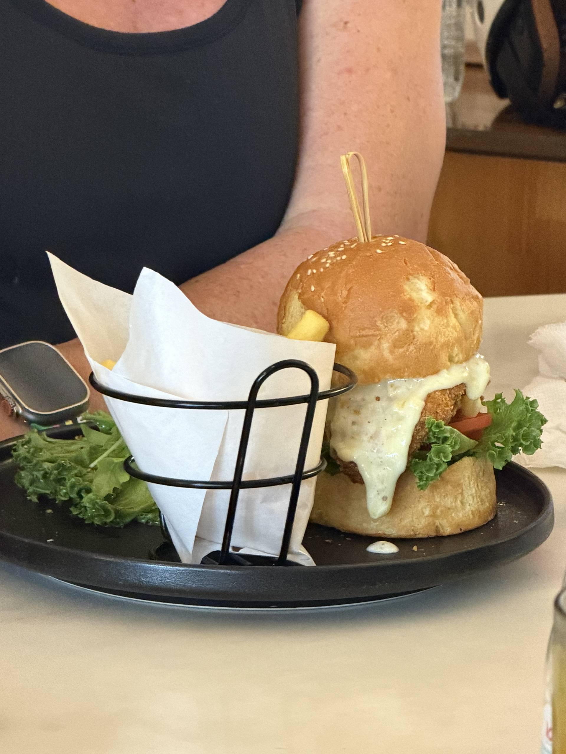 A close-up of a gourmet burger served with fries in a basket, placed on a black plate, suggesting a casual dining experience in Đà Lạt.