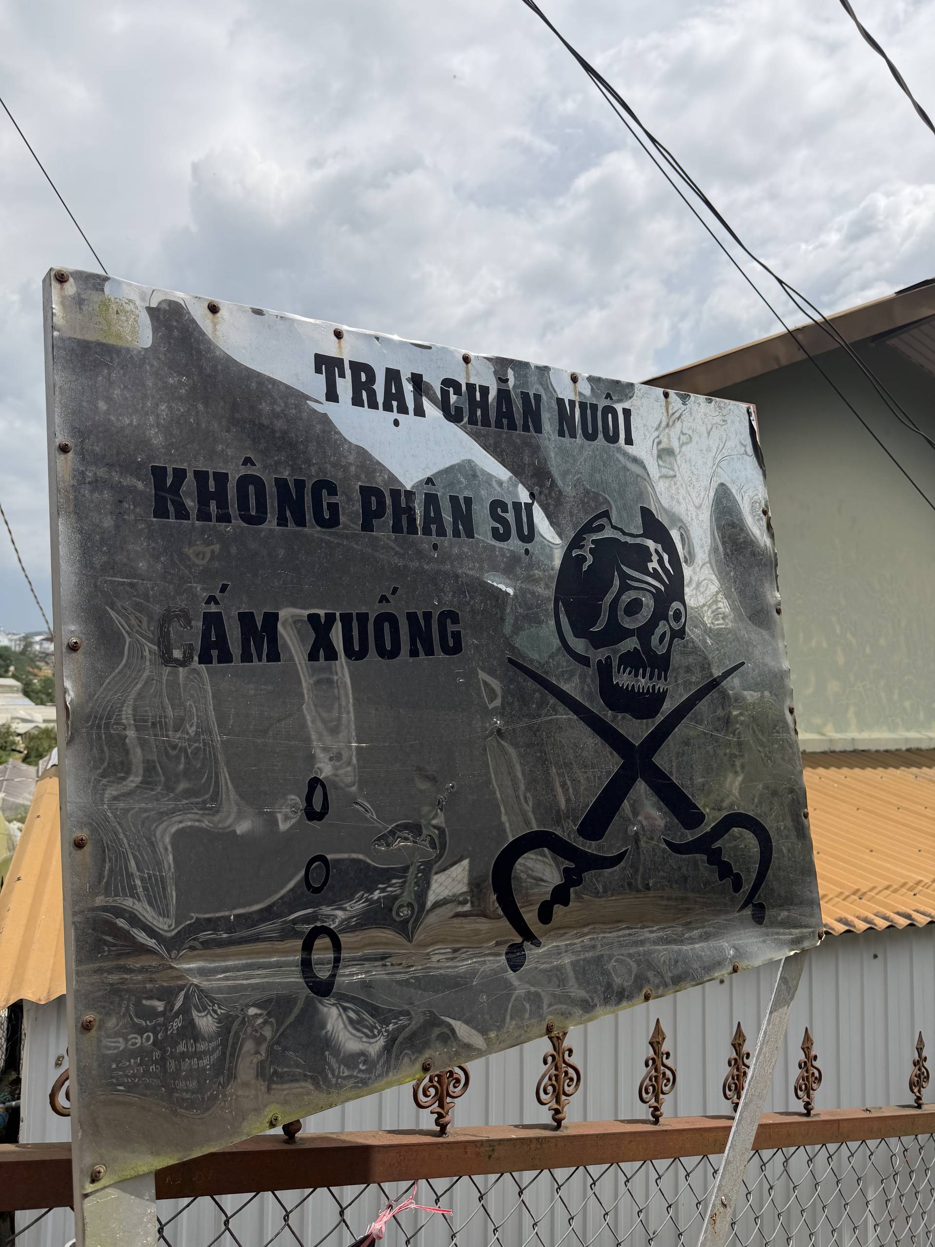 A signboard in Vietnamese with a skull and crossbones symbol, indicating a farm or animal breeding facility that does not discriminate against animals.