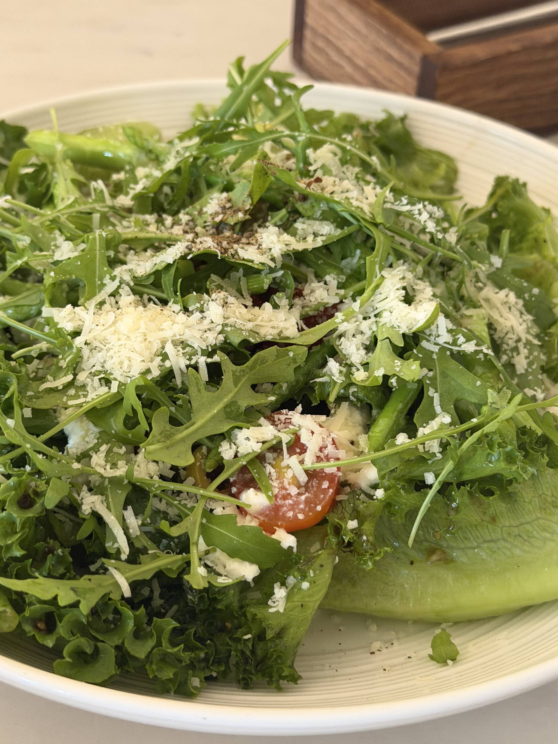 A fresh arugula salad topped with grated Parmesan cheese and cherry tomatoes, served in a white bowl at an event in Đà Lạt, Vietnam.