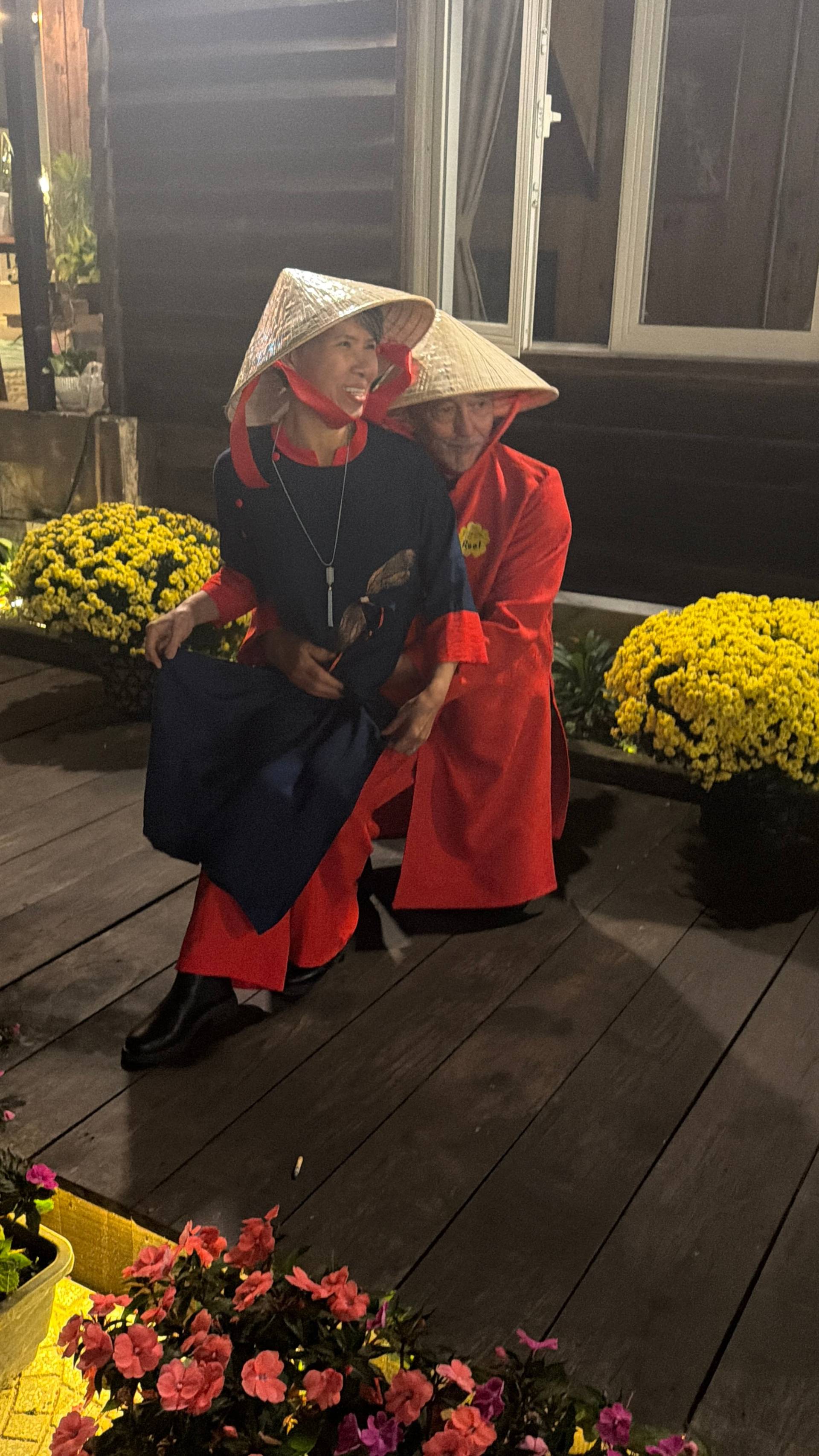 Evening garden celebration in Đà Lạt featuring figures in traditional dress and conical hats amid golden chrysanthemums. Nighttime patio event with warm lighting and authentic cultural ambiance.