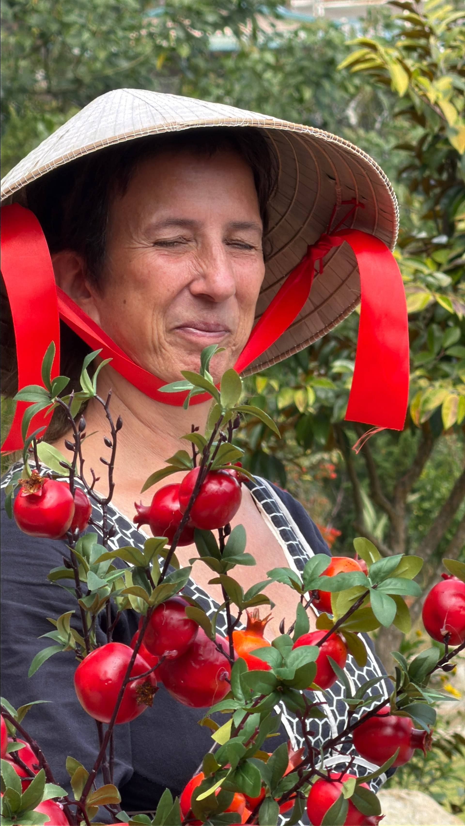 A harvest portrait in Đà Lạt's vibrant agricultural landscape. Tomato picking moment beneath conical hat and lush tropical foliage, showcasing local farming traditions.