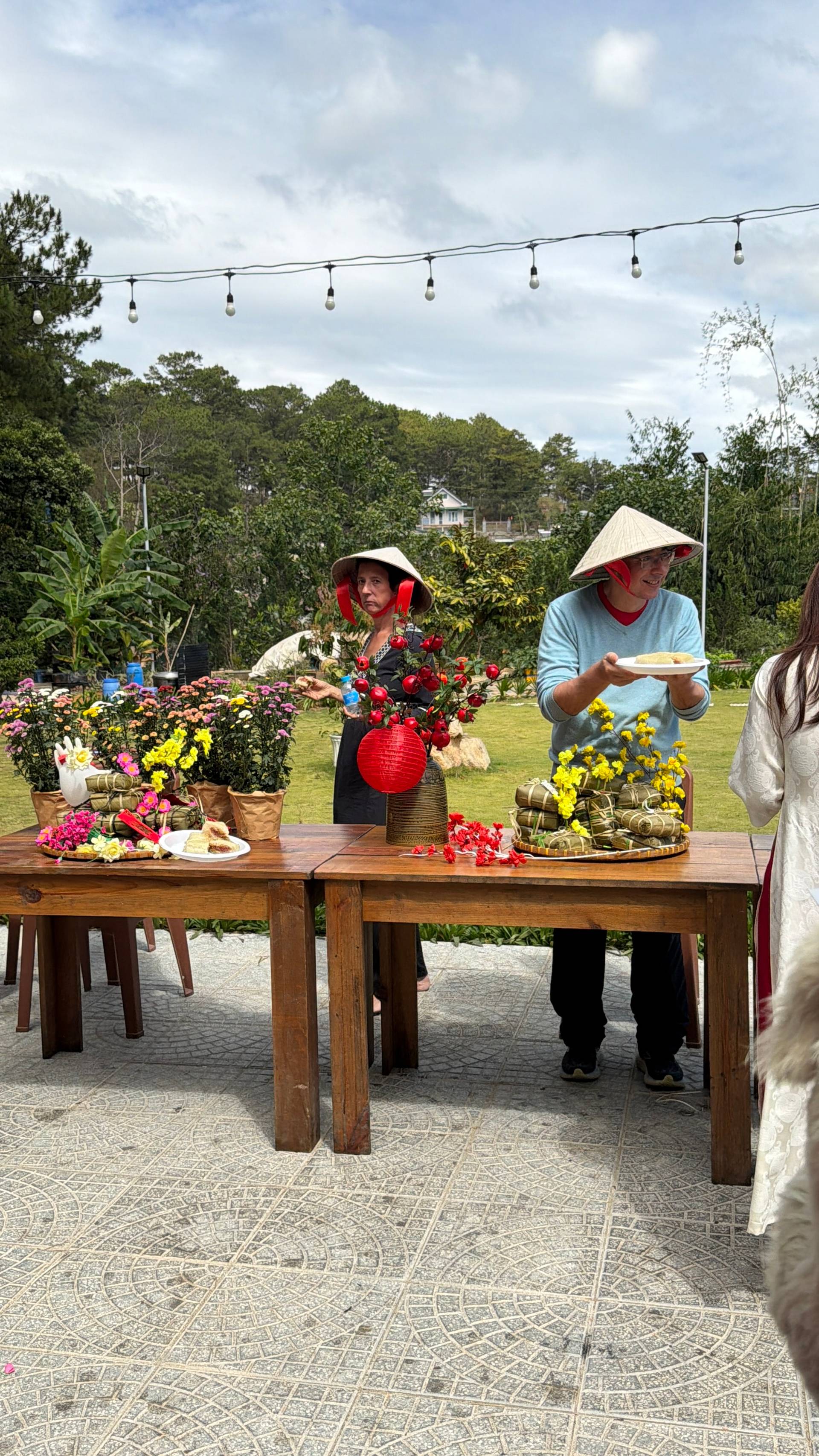 Outdoor garden party in Đà Lạt with traditional Vietnamese hospitality, featuring floral table arrangements, string lighting overhead, and forest backdrop, showcasing the city's signature blend of highland nature and cultural elegance.