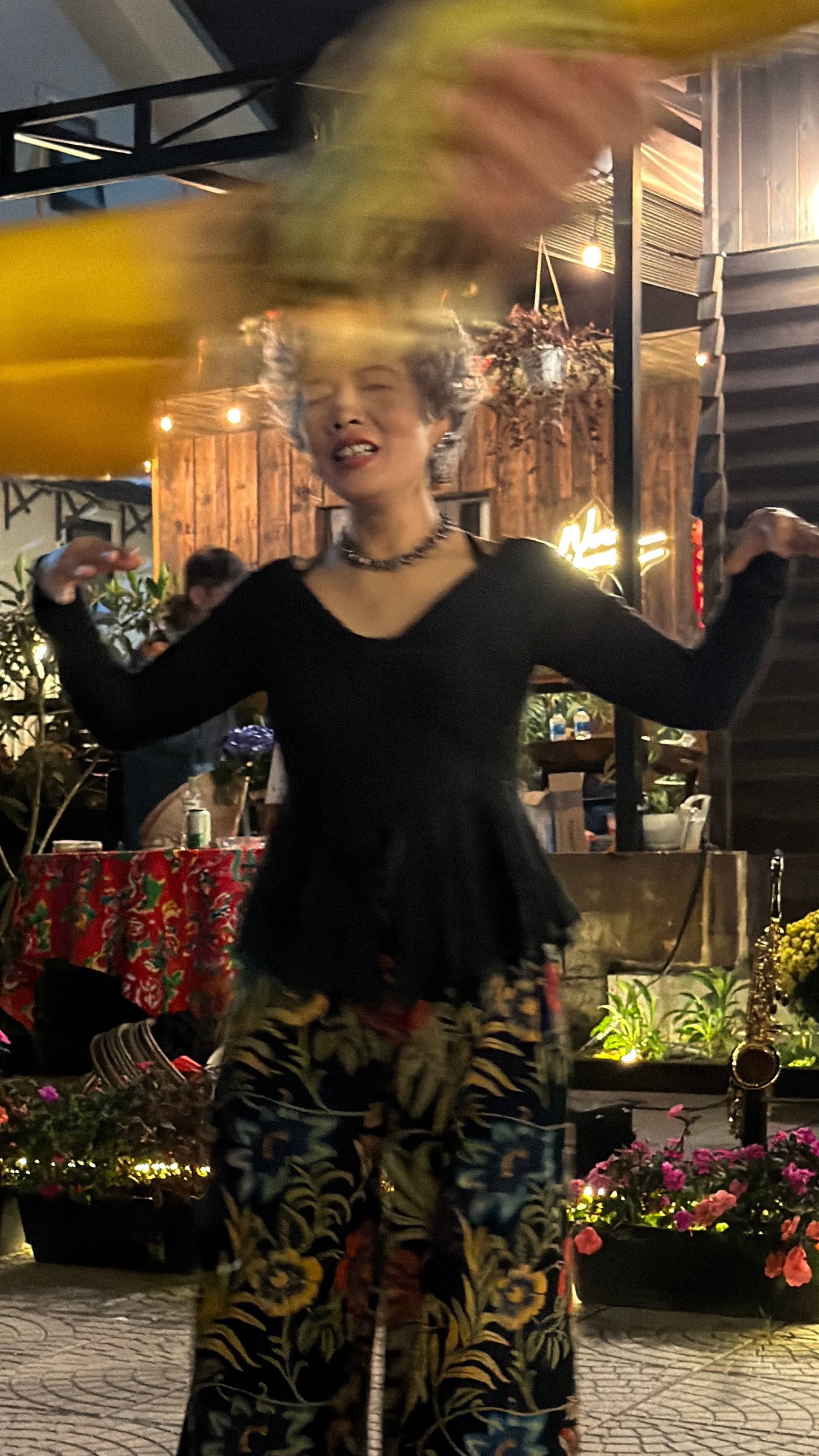 Indoor nighttime performance or entertainment at a Đà Lạt event, with participants in a decorated space featuring wooden architectural elements and flourishing plants, creating an intimate cultural gathering atmosphere.