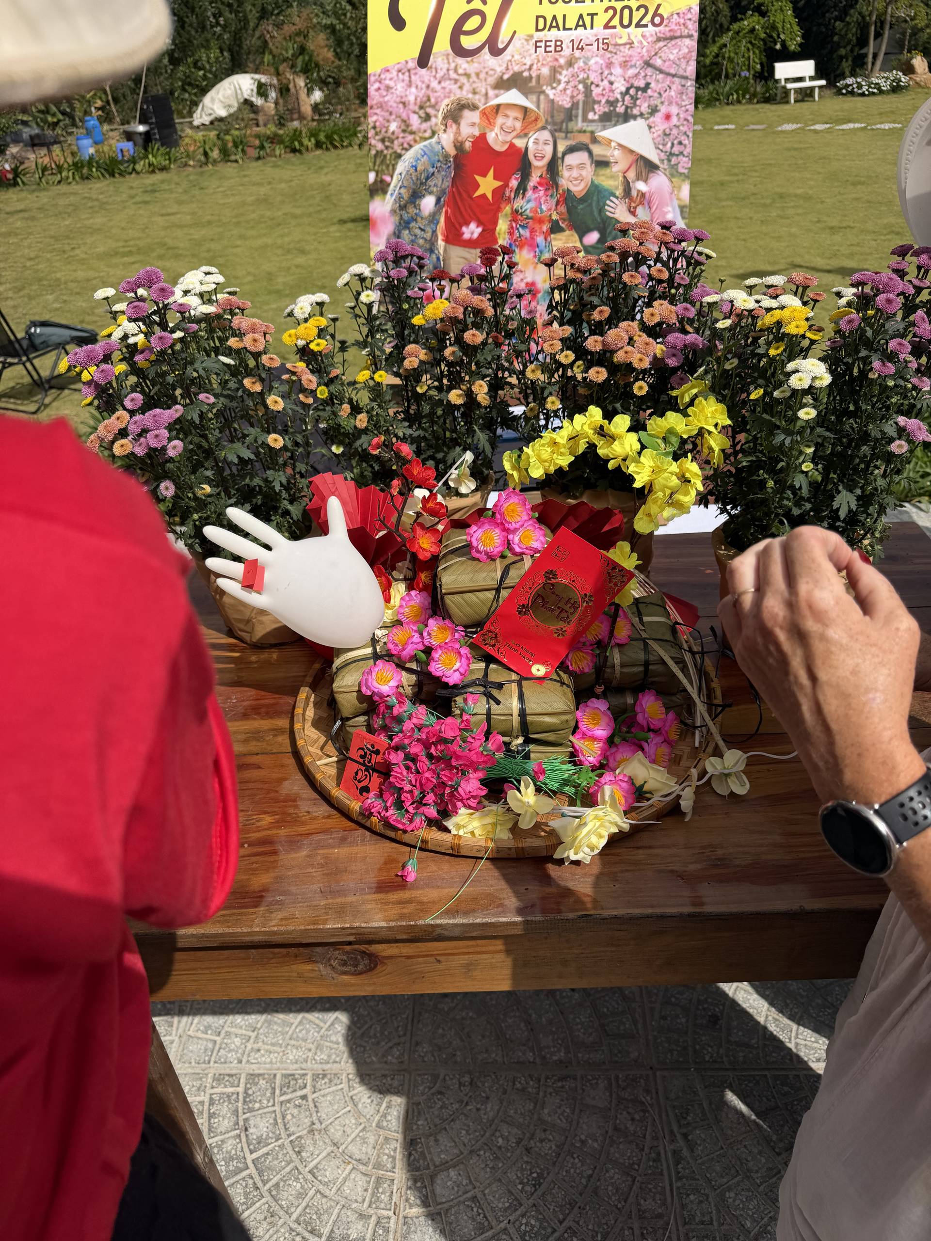 Vibrant flower display featuring carnations and chrysanthemums in pink, yellow, white, and orange at an outdoor Đà Lạt festival. Traditional Vietnamese decor and wooden platform setup with festive backdrop.