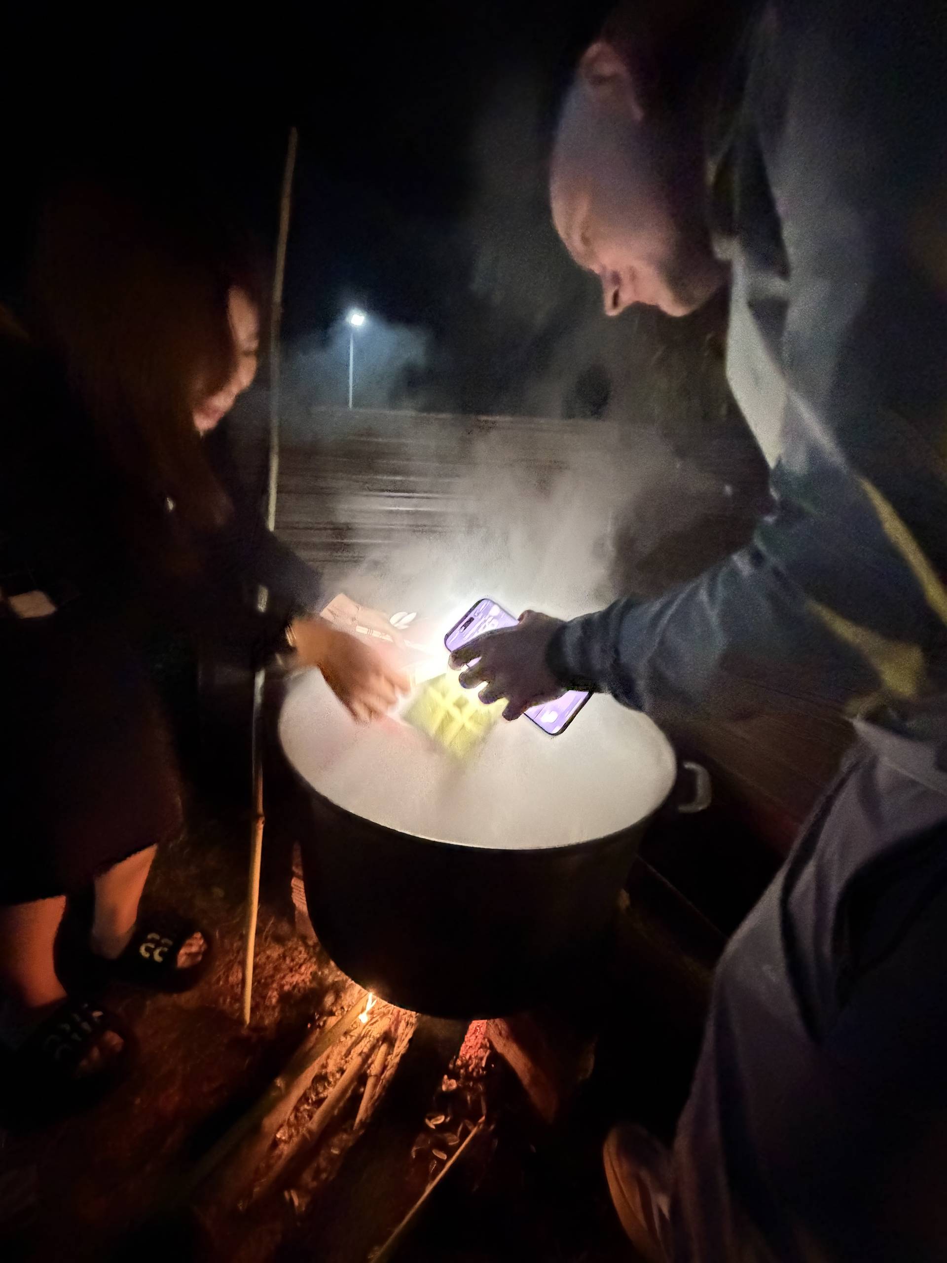 Evening food demonstration event in Đà Lạt featuring interactive cooking activity around a large white plate. Guests gather under string lights to participate in hands-on culinary experience during nighttime garden celebration.