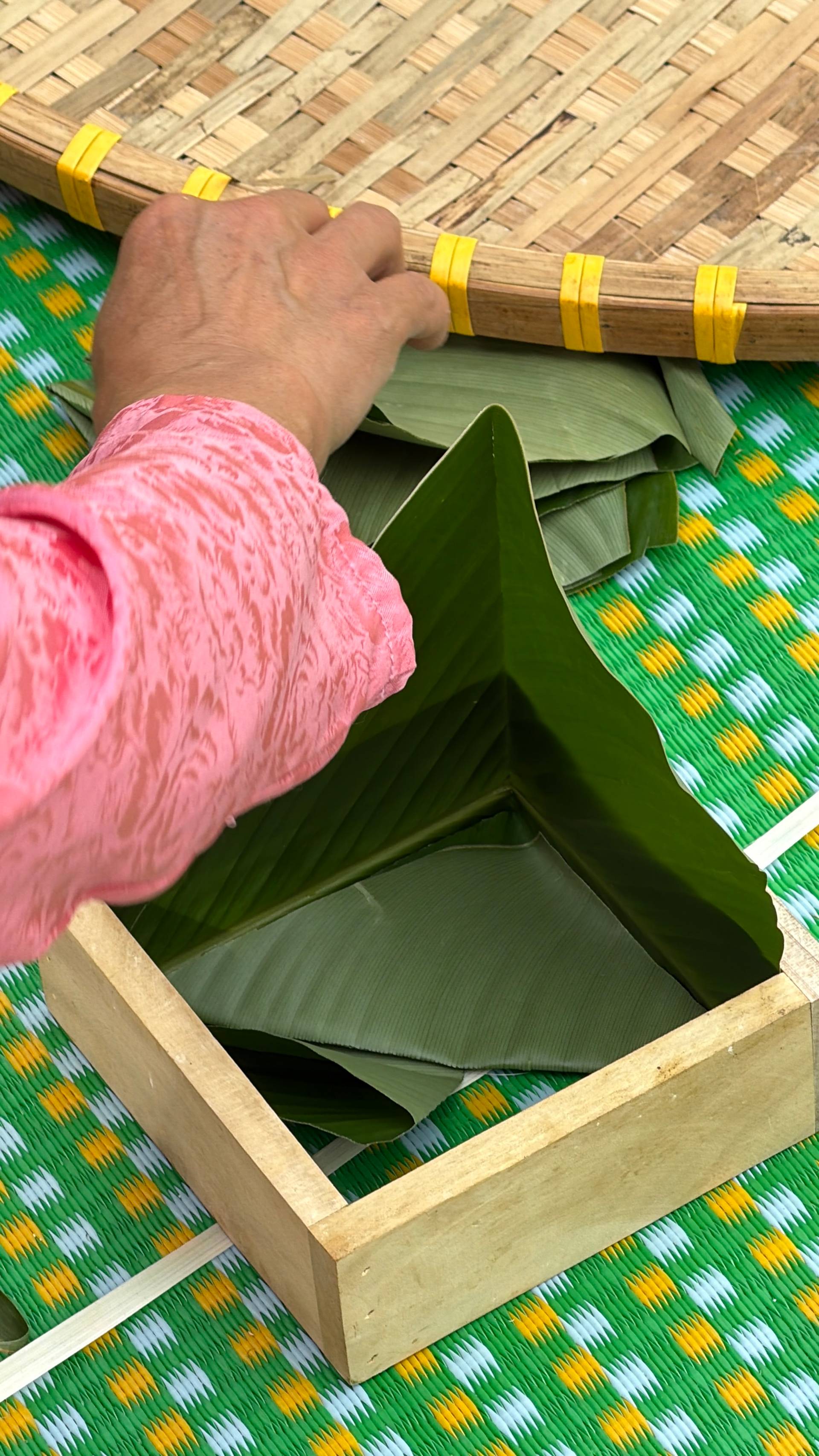 Close-up detail of traditional conical hat weaving process showing bamboo strips with yellow binding and fresh straw materials on vibrant Vietnamese textile background.