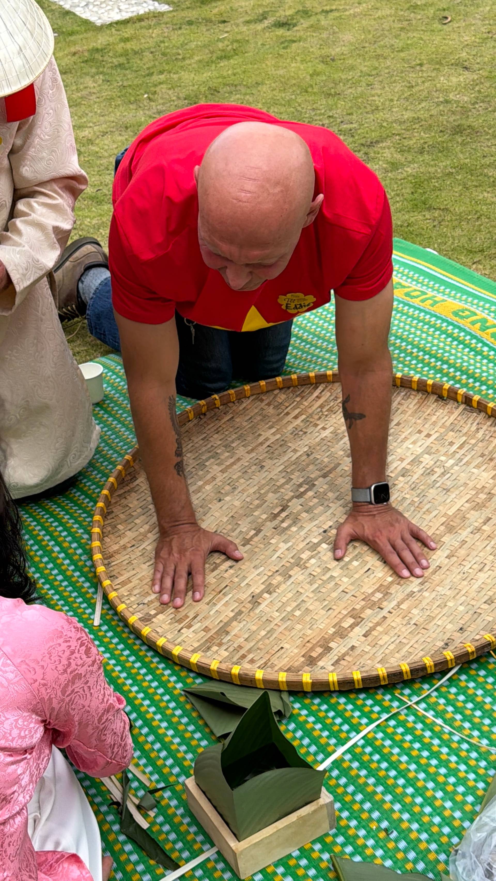 Traditional Vietnamese conical hat weaving demonstration at a Đà Lạt event, showing hands-on craft activity with woven bamboo frames and yellow binding on colorful patterned textile.