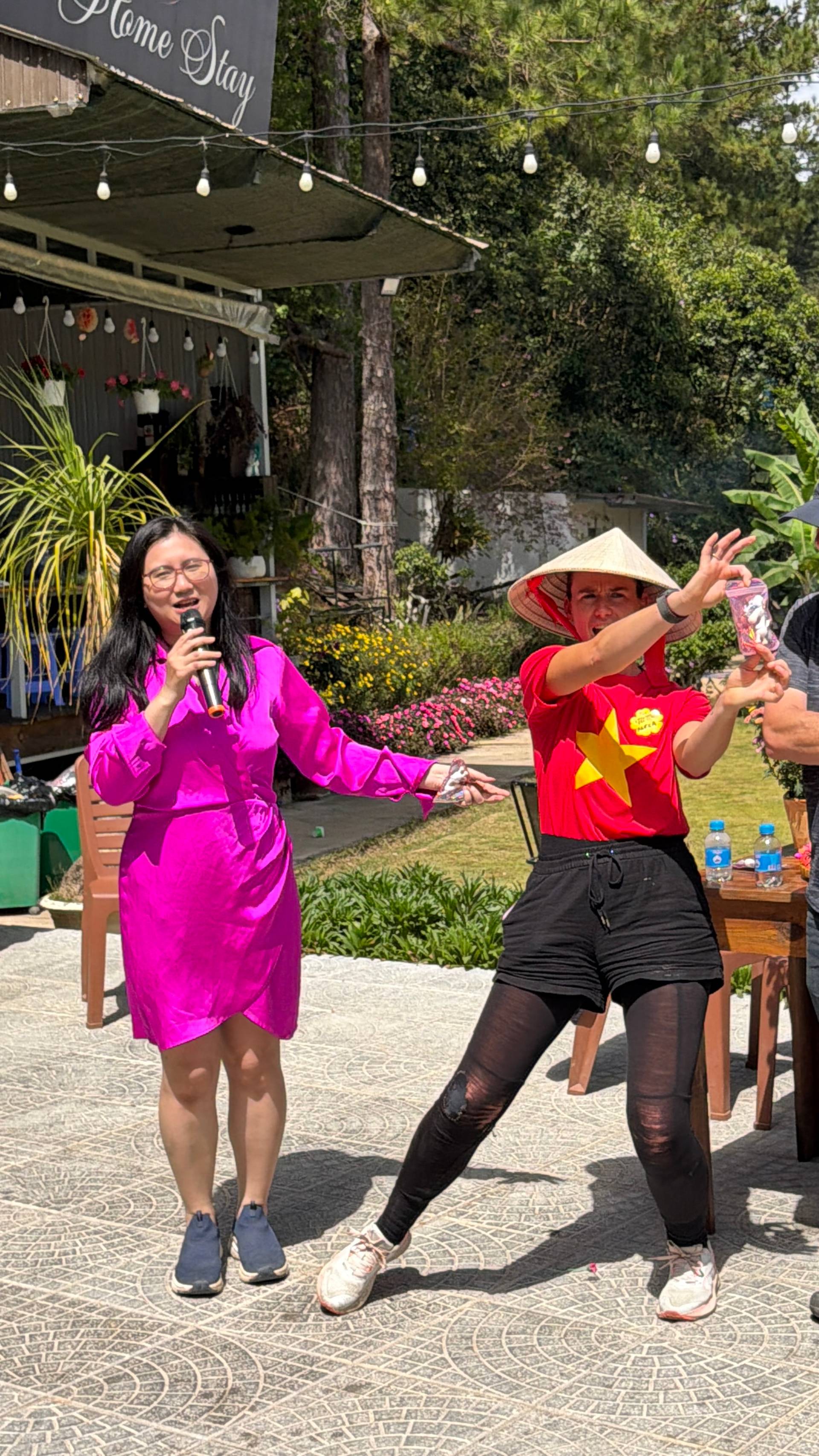 Event hosting at a Đà Lạt venue with traditional conical hats, outdoor stage setup, and colorful signage in a garden setting with decorative flowers and lighting.