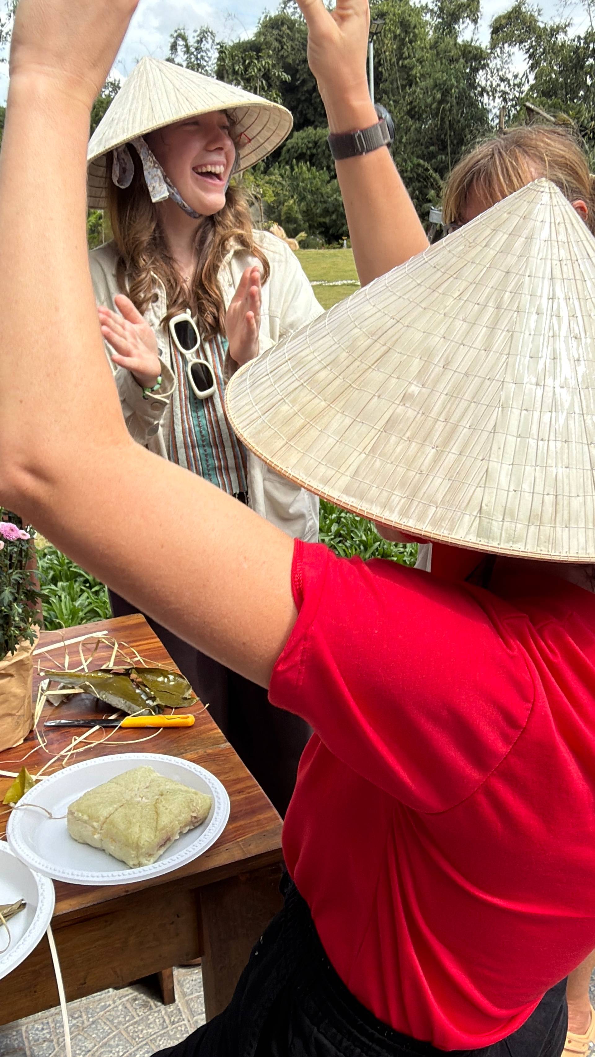 Joyful celebration with traditional Vietnamese conical hats and steamed rice cake, captured in a sunny garden setting with guests expressing happiness and cultural pride.