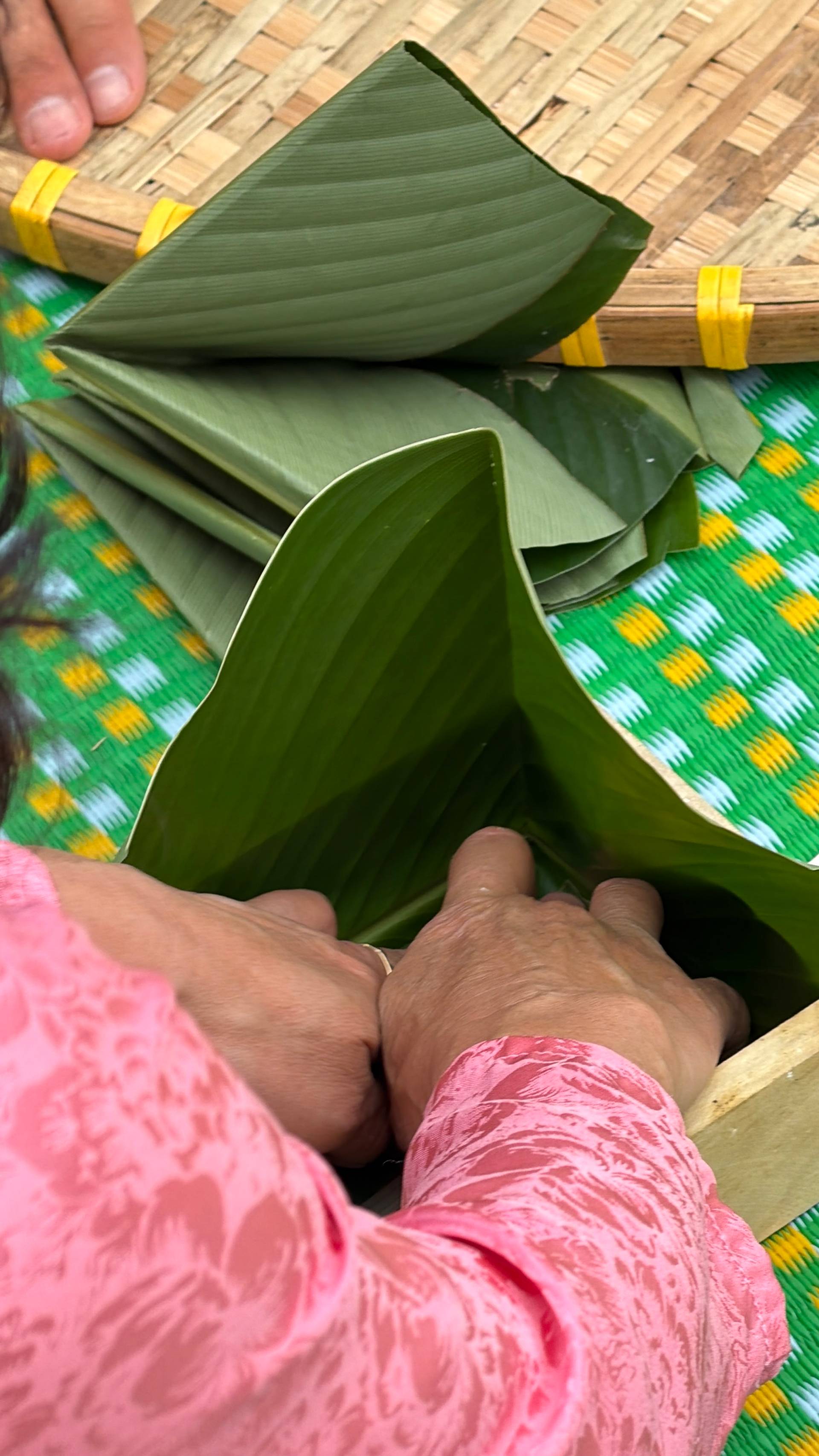A close-up demonstration of traditional Vietnamese banana leaf folding technique, showing hands at work on a colorful patterned textile backdrop.