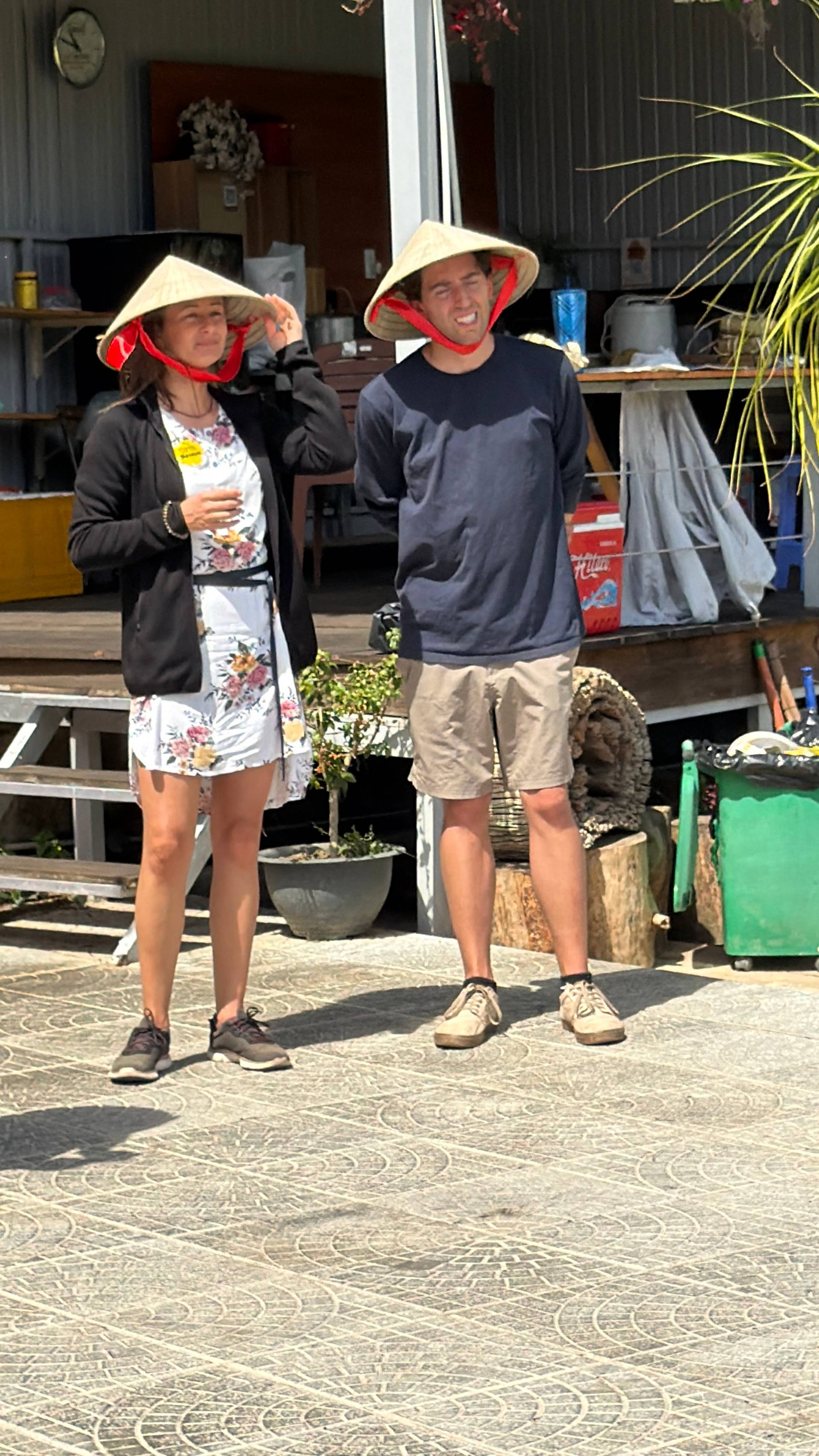 A joyful moment at a Đà Lạt event with visitors wearing iconic red-lined conical hats (nón lá) at a rustic wooden venue, capturing the essence of traditional Vietnamese culture.