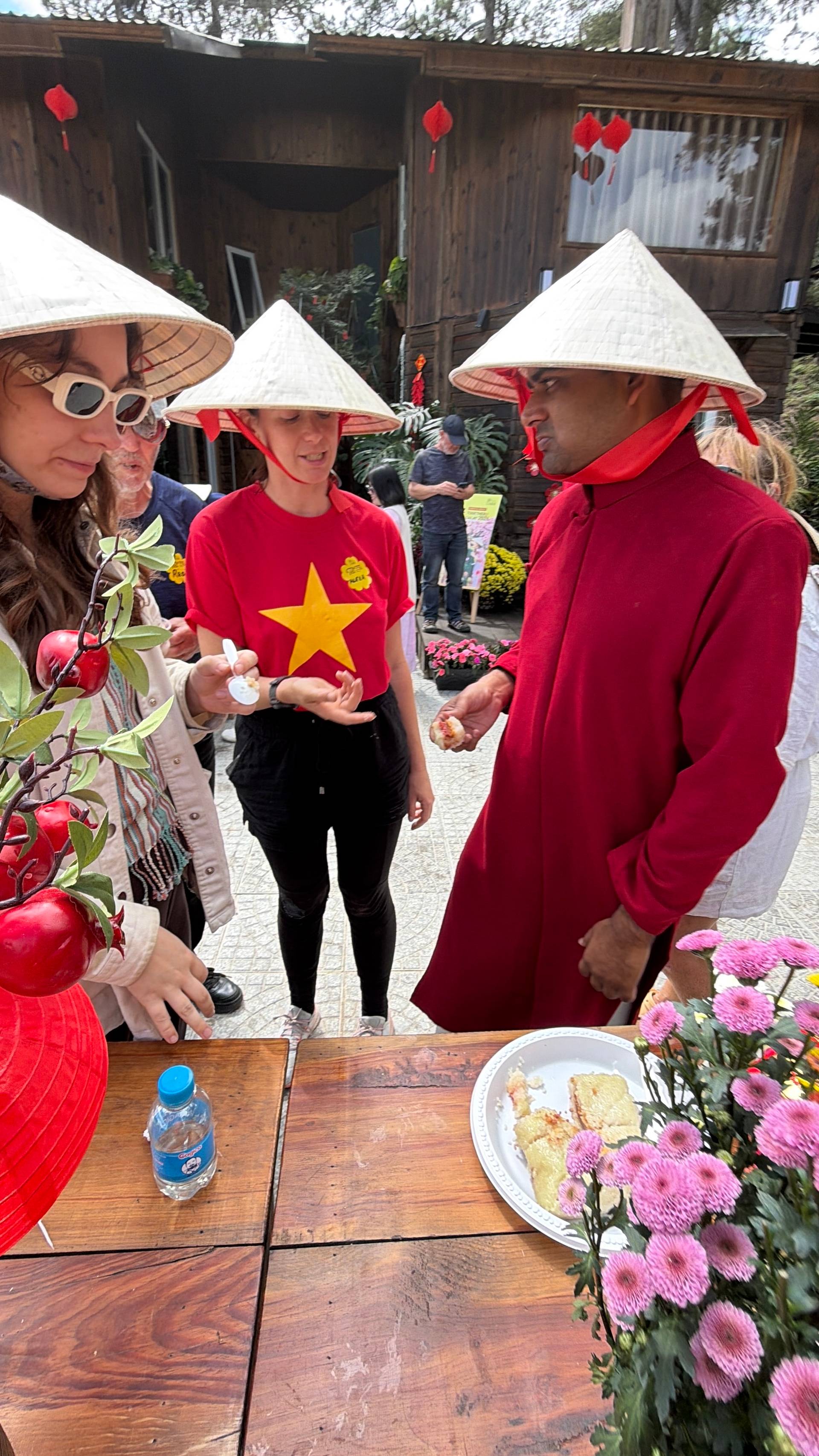 Traditional Vietnamese cultural event in Đà Lạt with conical nón lá hats, red lanterns, rustic wooden structures, and decorative pink flowers at an outdoor garden venue.