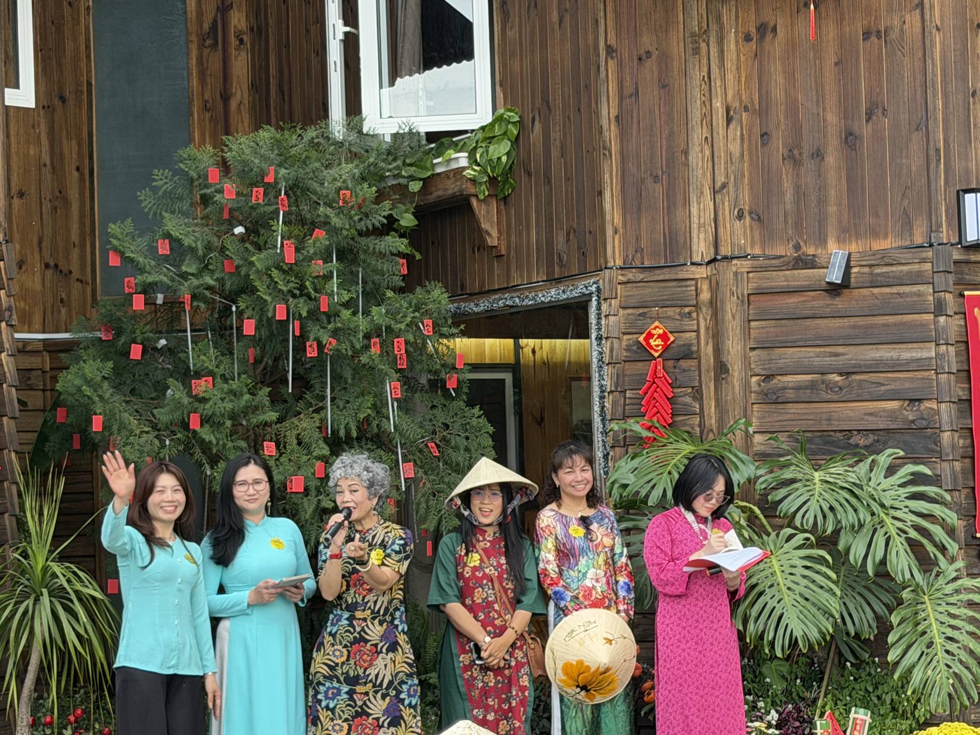 Group gathered in traditional Vietnamese dress in front of a historic wooden structure decorated with red lanterns and a large decorative plant installation in Đà Lạt.