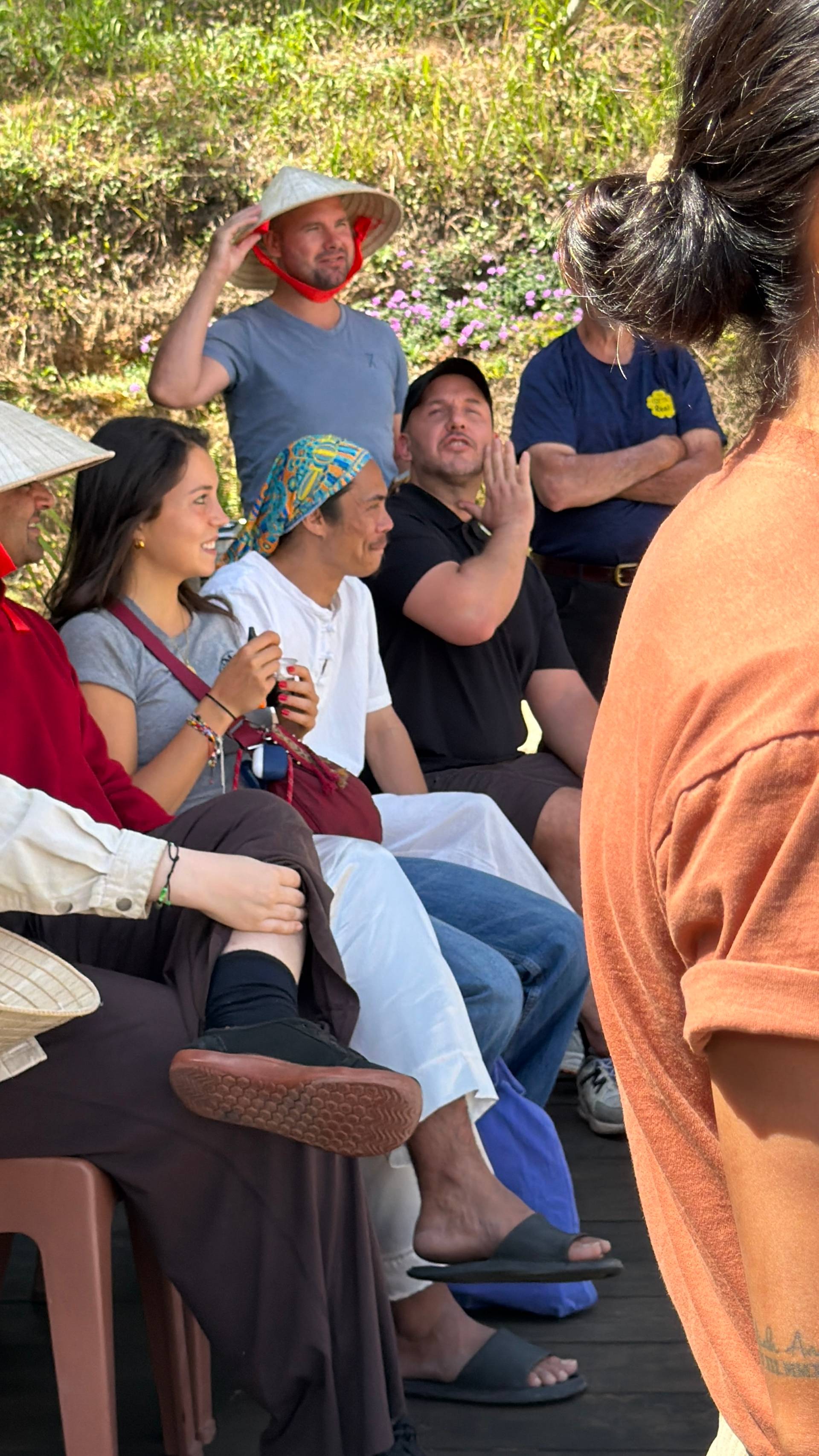 Group of visitors seated in a garden setting during an interactive presentation or workshop, surrounded by blooming flowers and tropical plants in Đà Lạt.