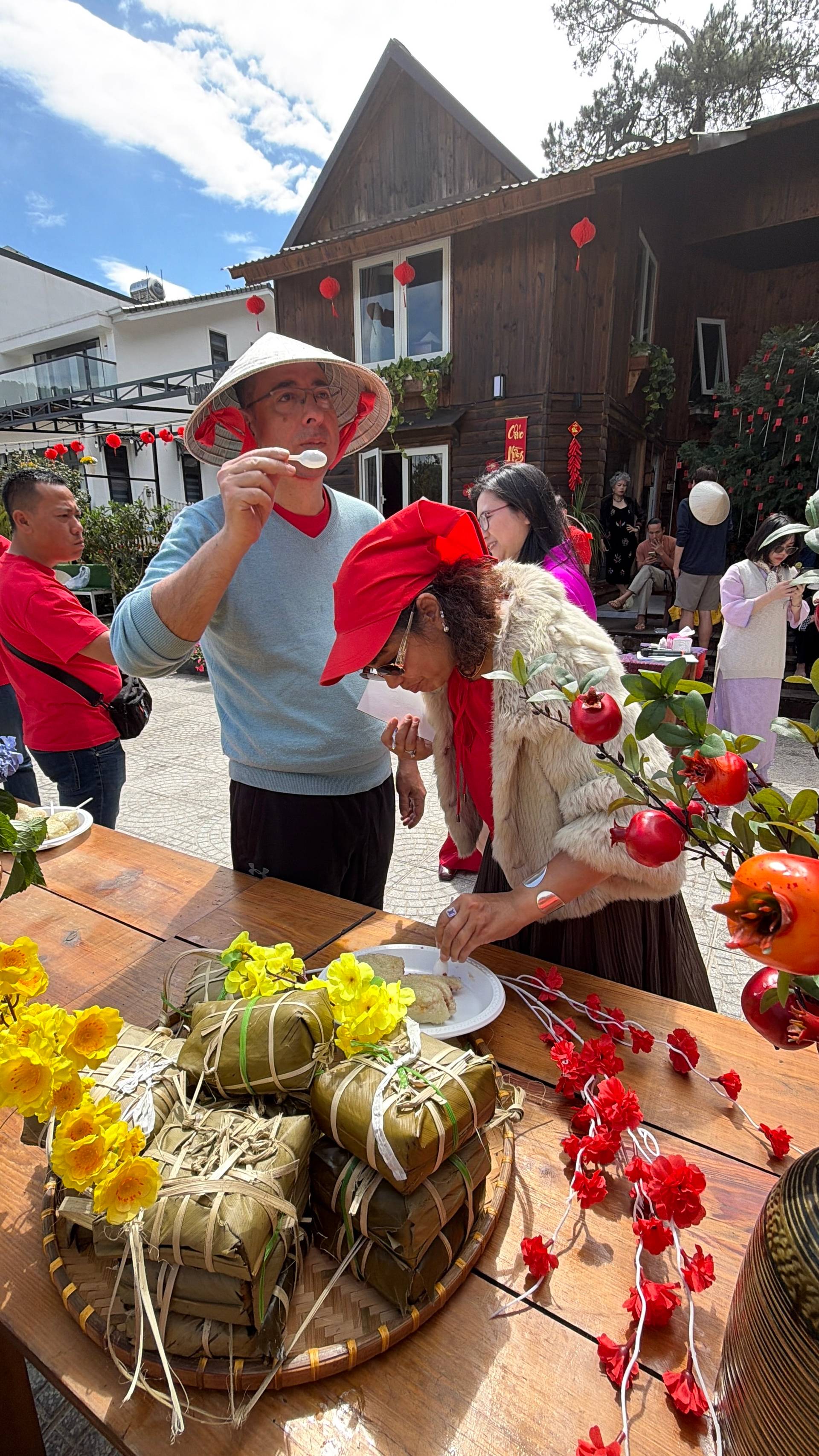 Person speaking at an outdoor event in Đà Lạt's distinctive pine forest setting, delivering a presentation or message during daytime celebration. Mountain backdrop with coniferous trees creates authentic regional atmosphere.