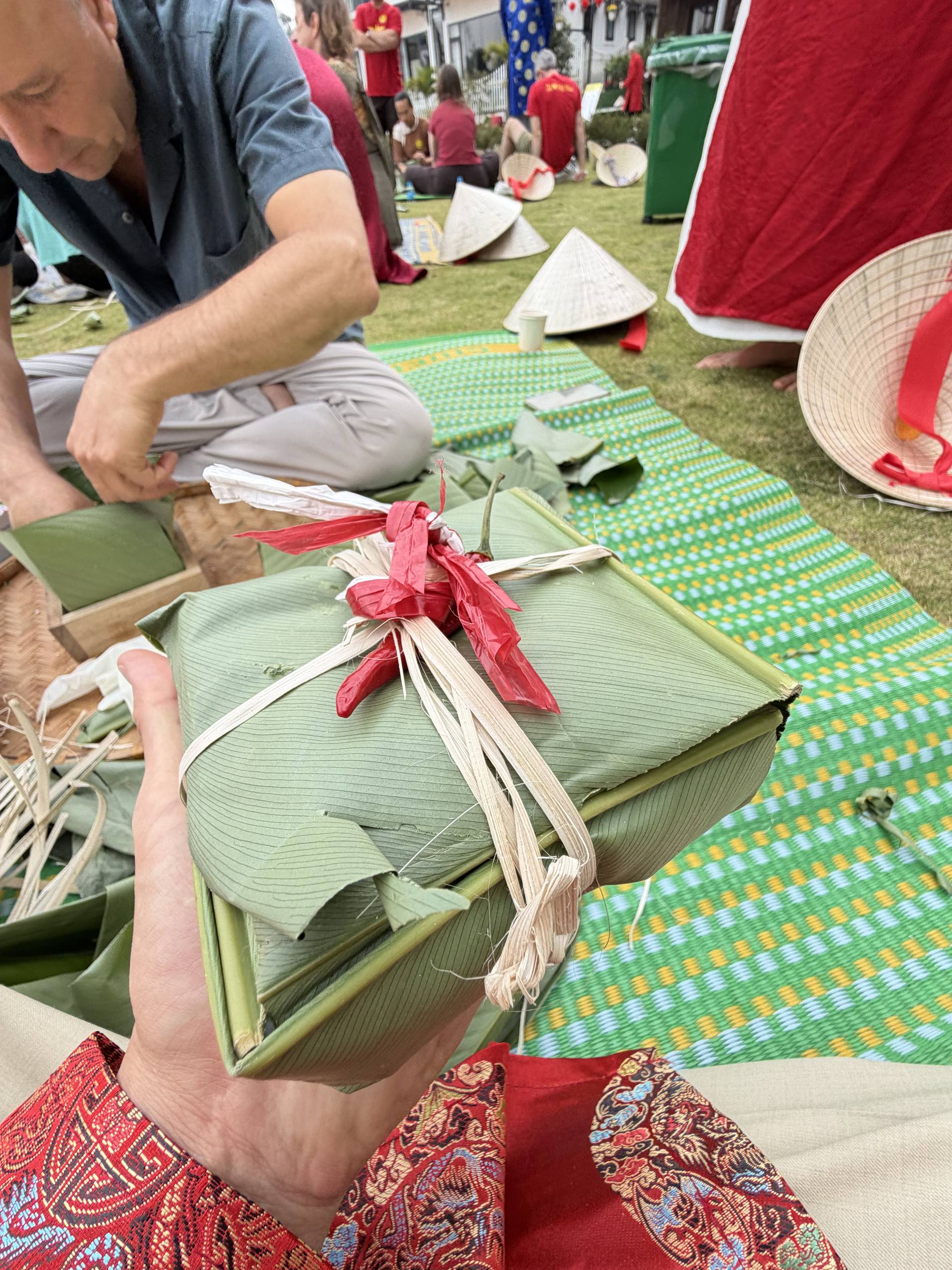 Hands folding traditional bánh chưng (sticky rice cakes) wrapped in green banana leaves and tied with red ribbons during a Tet workshop at a Đà Lạt cultural celebration.