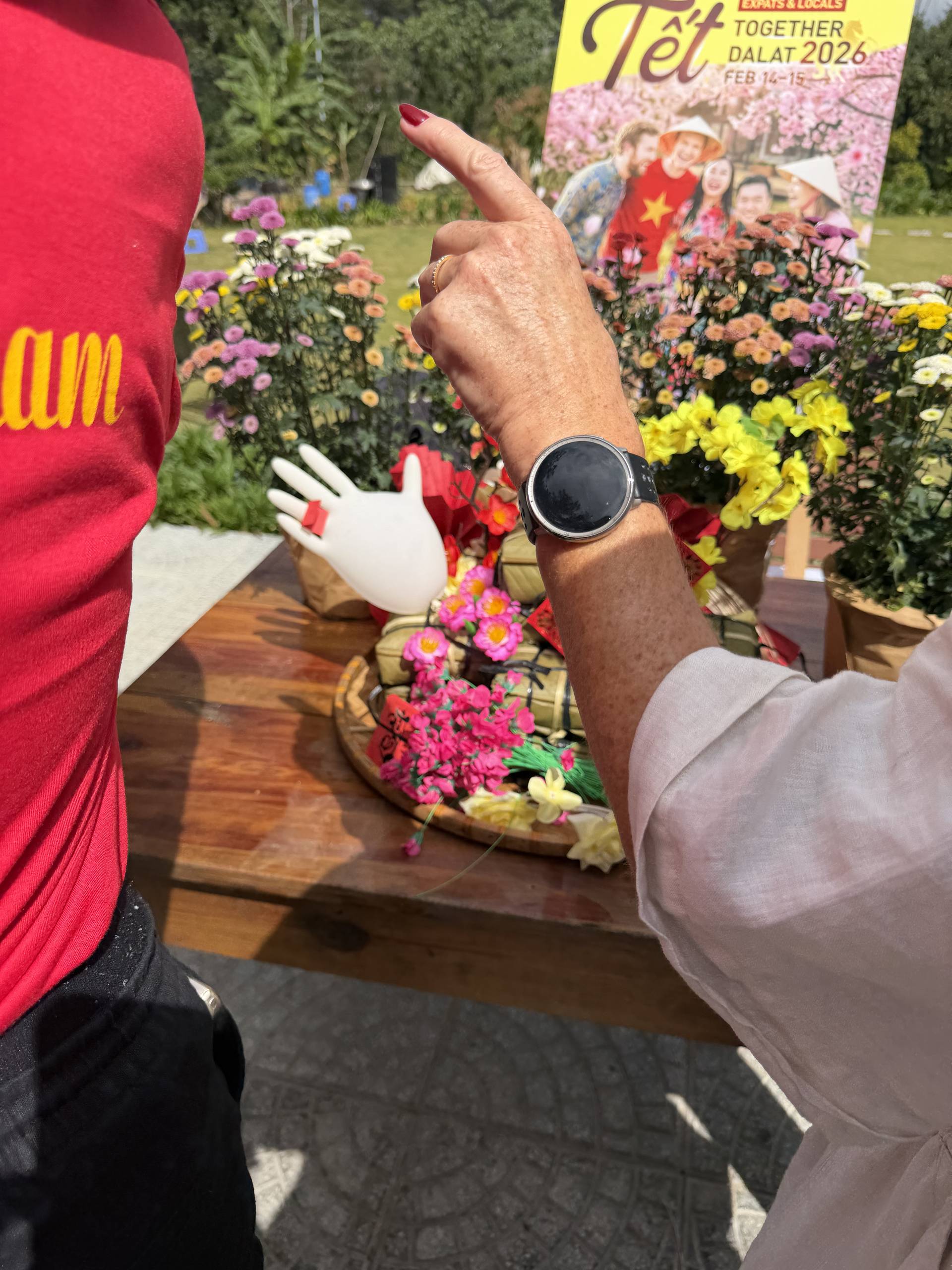 A close-up of hands during the Tet Together Dalat 2026 festival, pointing at vibrant chrysanthemums and festive decorations at a community celebration event.