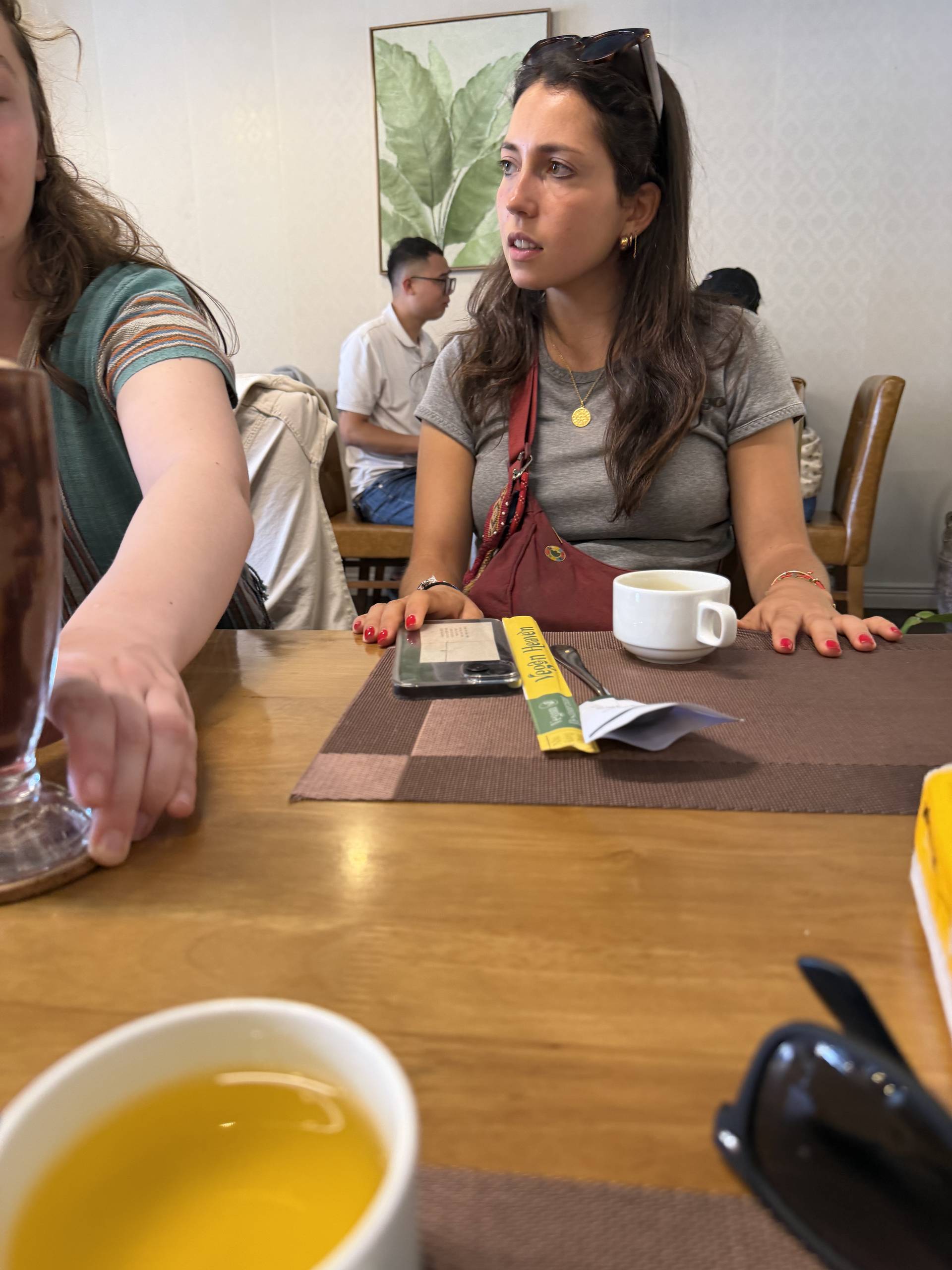 An indoor discussion or tea tasting event at a Tet celebration, with participants gathered around a wooden table with tea service, coffee, and educational materials.
