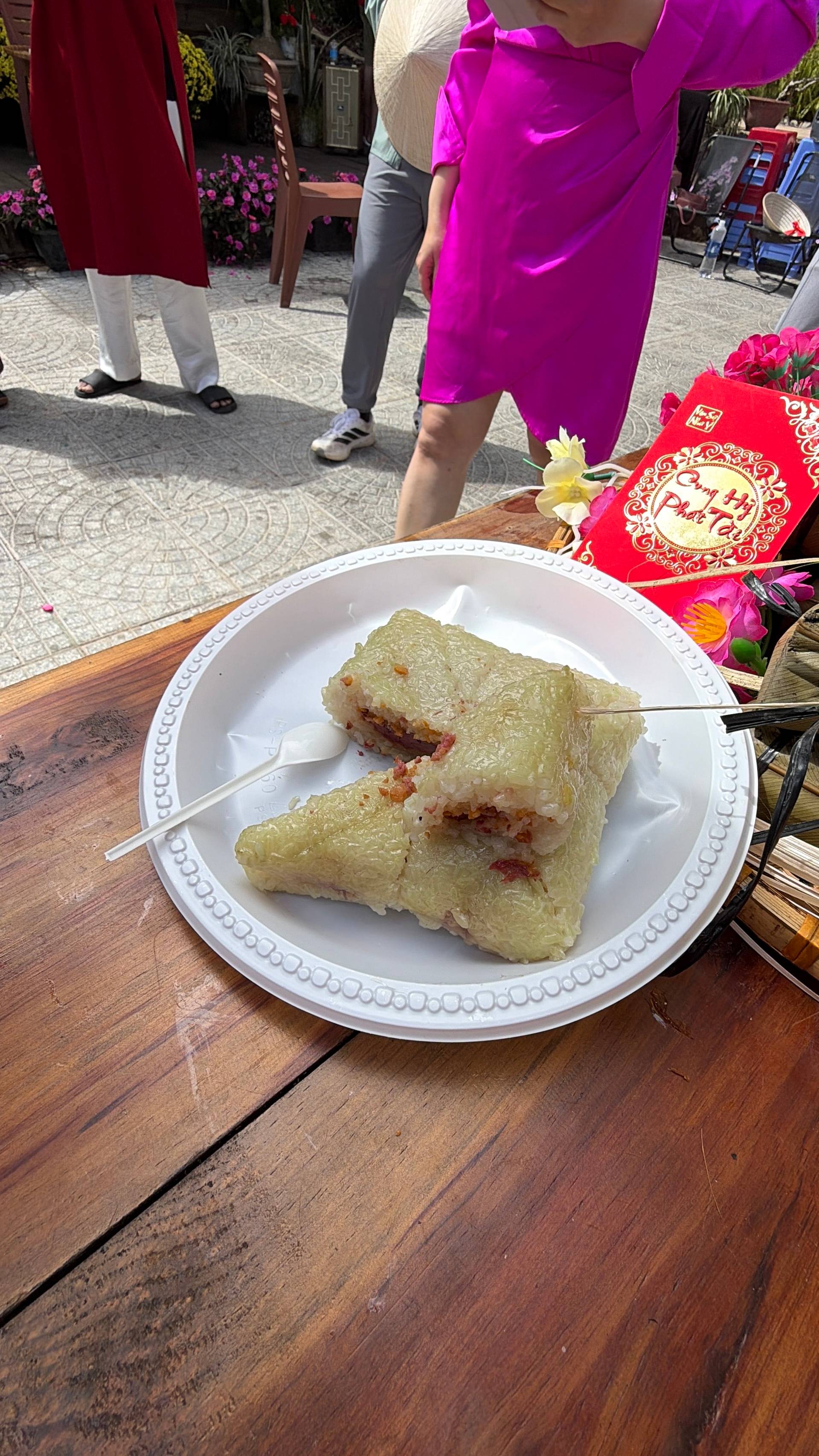 Traditional bánh chưng (square sticky rice cake with red filling) served at a Tet celebration in Đà Lạt, accompanied by festive red decorations and colorful flowers on a wooden table.