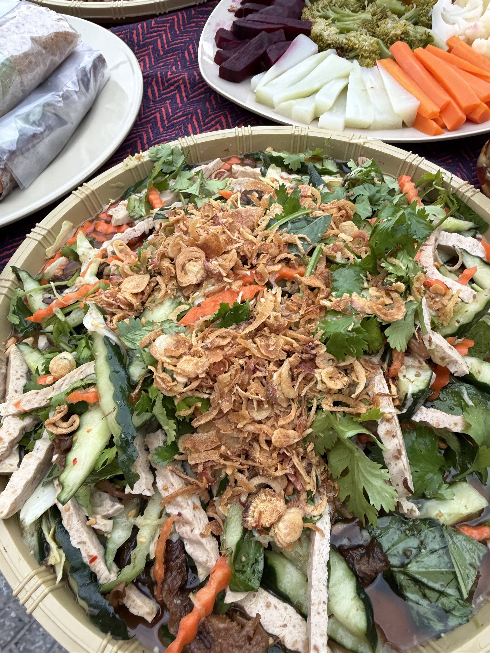 Vietnamese salad dish with crispy shallots, fresh herbs, sliced vegetables, and protein served on a white plate with accompanying vegetable sides.