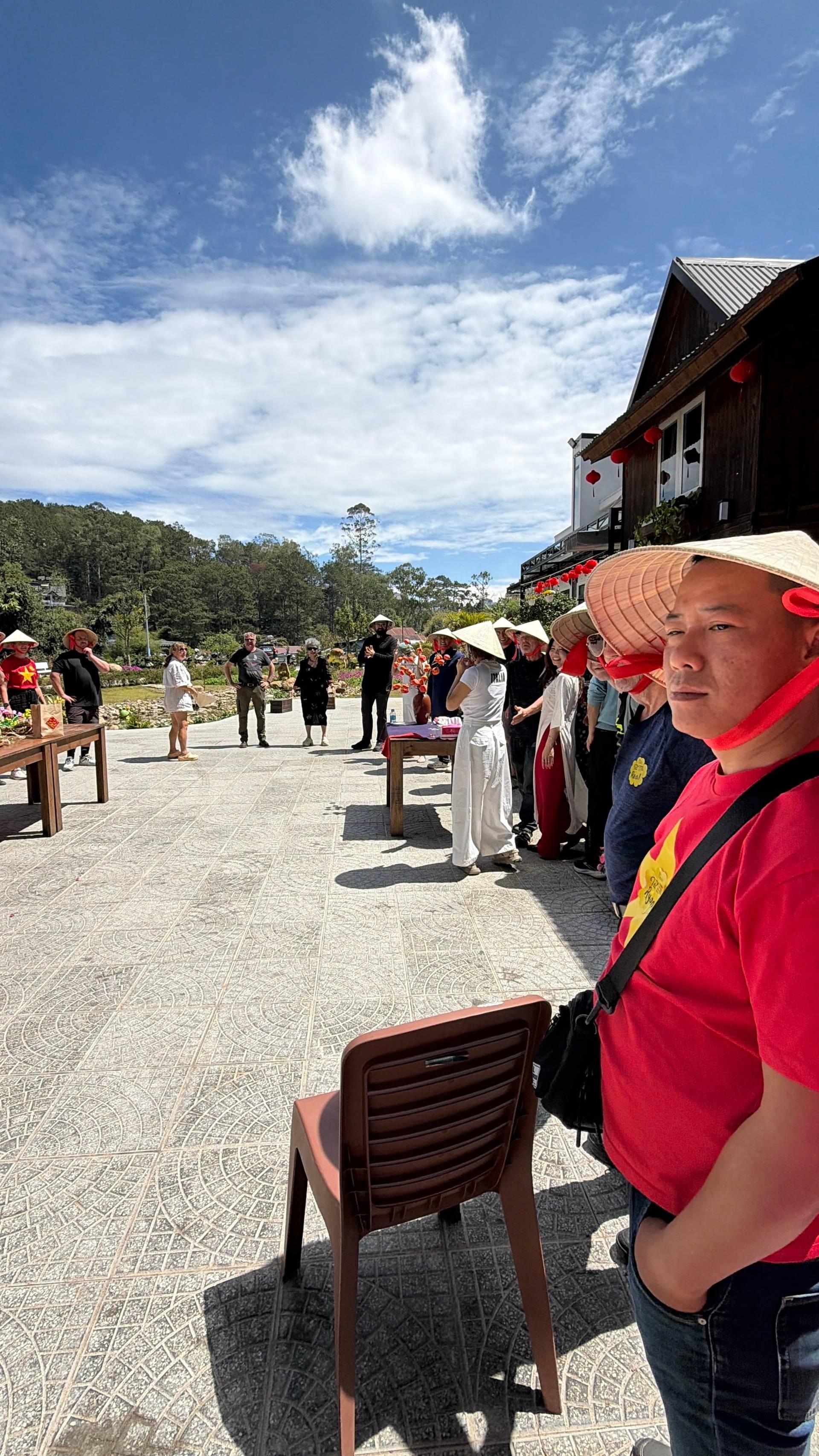 Daytime cultural celebration in Đà Lạt's pine highlands featuring participants in traditional áo dài and conical hats at a rural event venue.
