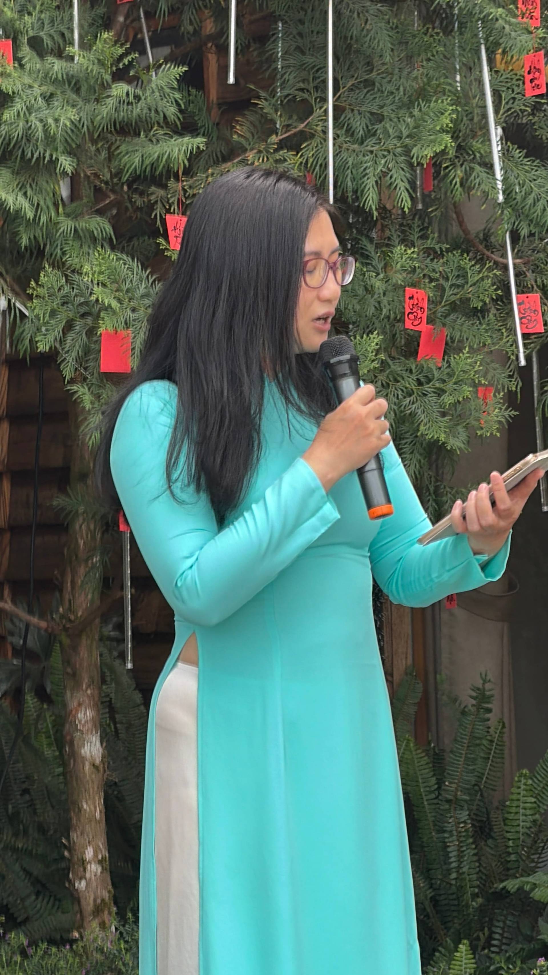 A speaker at a microphone during a presentation event in Đà Lạt, with traditional Vietnamese décor including red lanterns and decorative greenery.